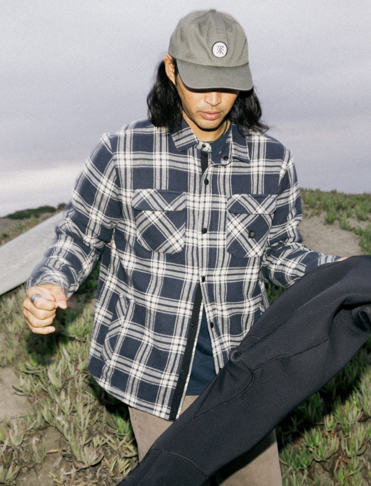 Man dressed in adventure essentials with a plaid shirt, denim jacket, and cap, ready for outdoor exploration.
