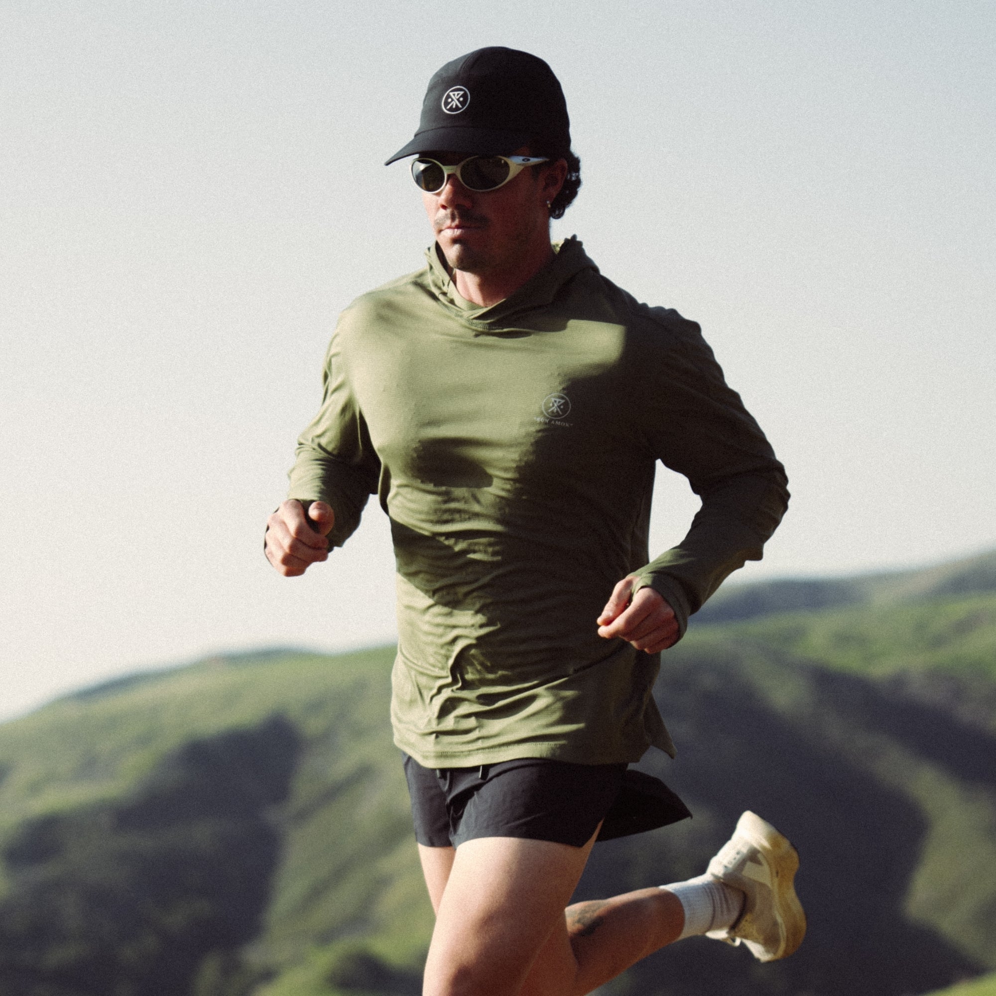 Adventurous individual wearing the Roark Alta Elite Trail Long Sleeve Tee, equipped with sunglasses and a hat, enjoying outdoor recreation.