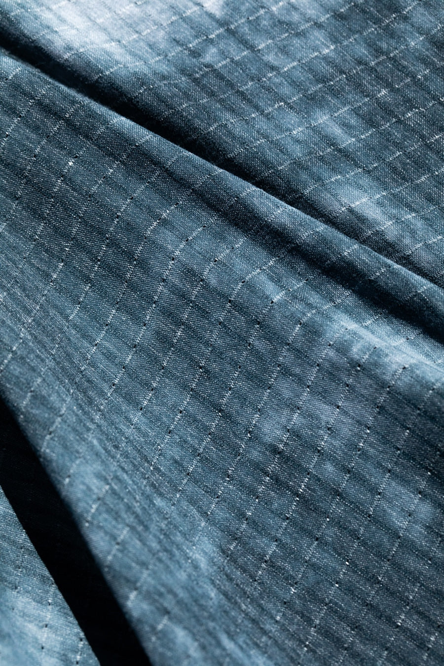 Slate blue HOLEYTECH fabric with perforated texture and diagonal fold creating dimensional shadow detail