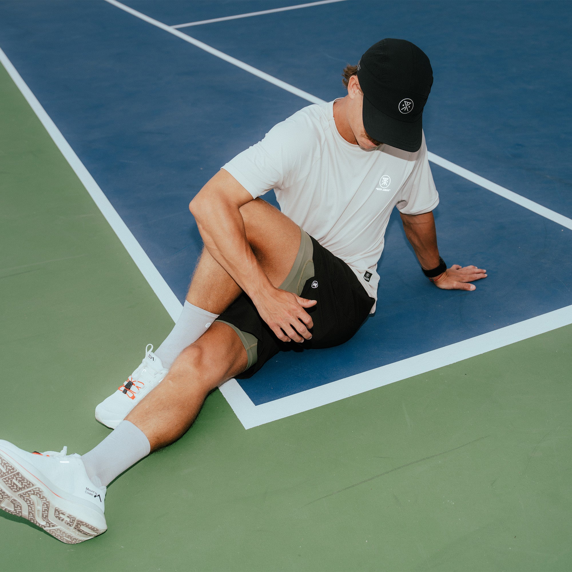 Man wearing white Alta Elite Trail short sleeve tee on blue and green tennis court during match play