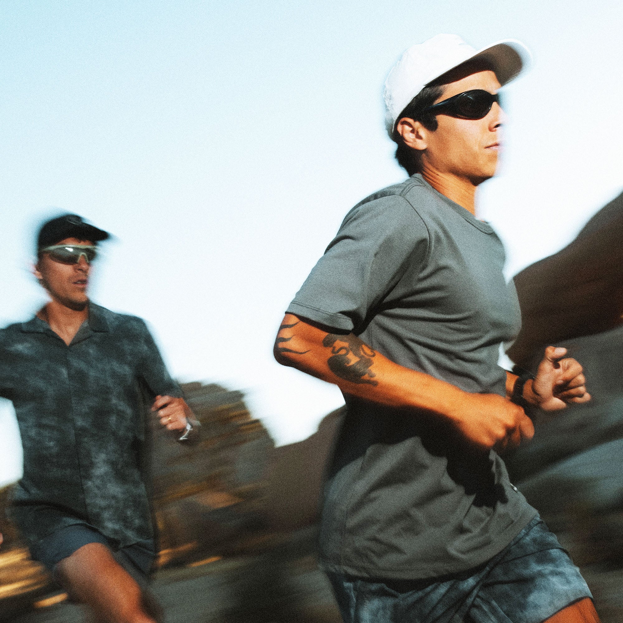 Man wearing gray Alta Elite trail short sleeve tee with white cap and black sunglasses running outdoors