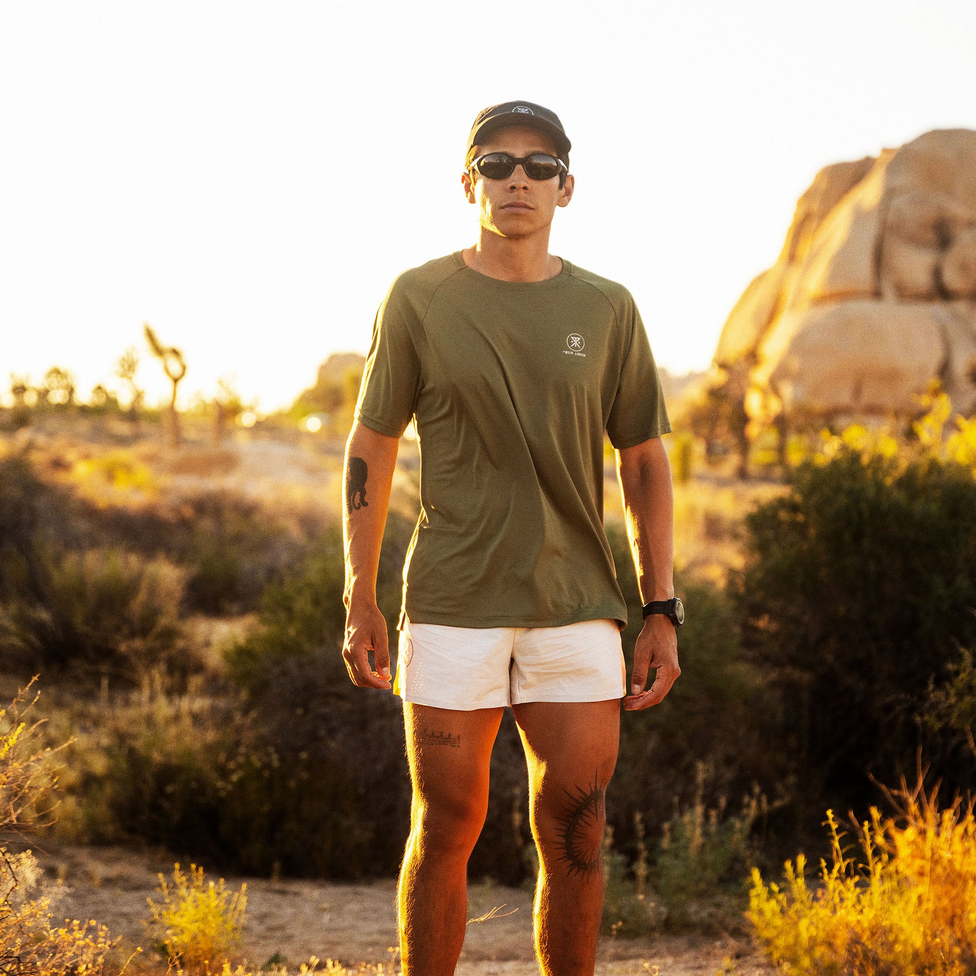 Man wearing light military green Alta Elite Trail short sleeve tee and white shorts in desert landscape at sunset