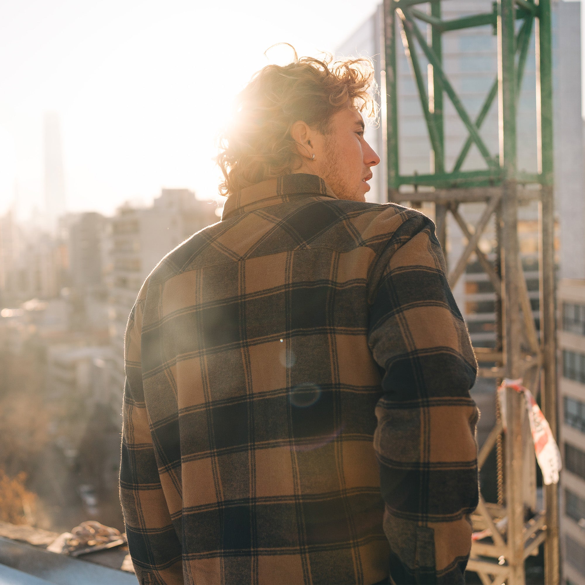 Man wearing Roark's Backwoods Overshirt Jacket in plaid pattern, exploring the urban environment with high-rise buildings in the background.