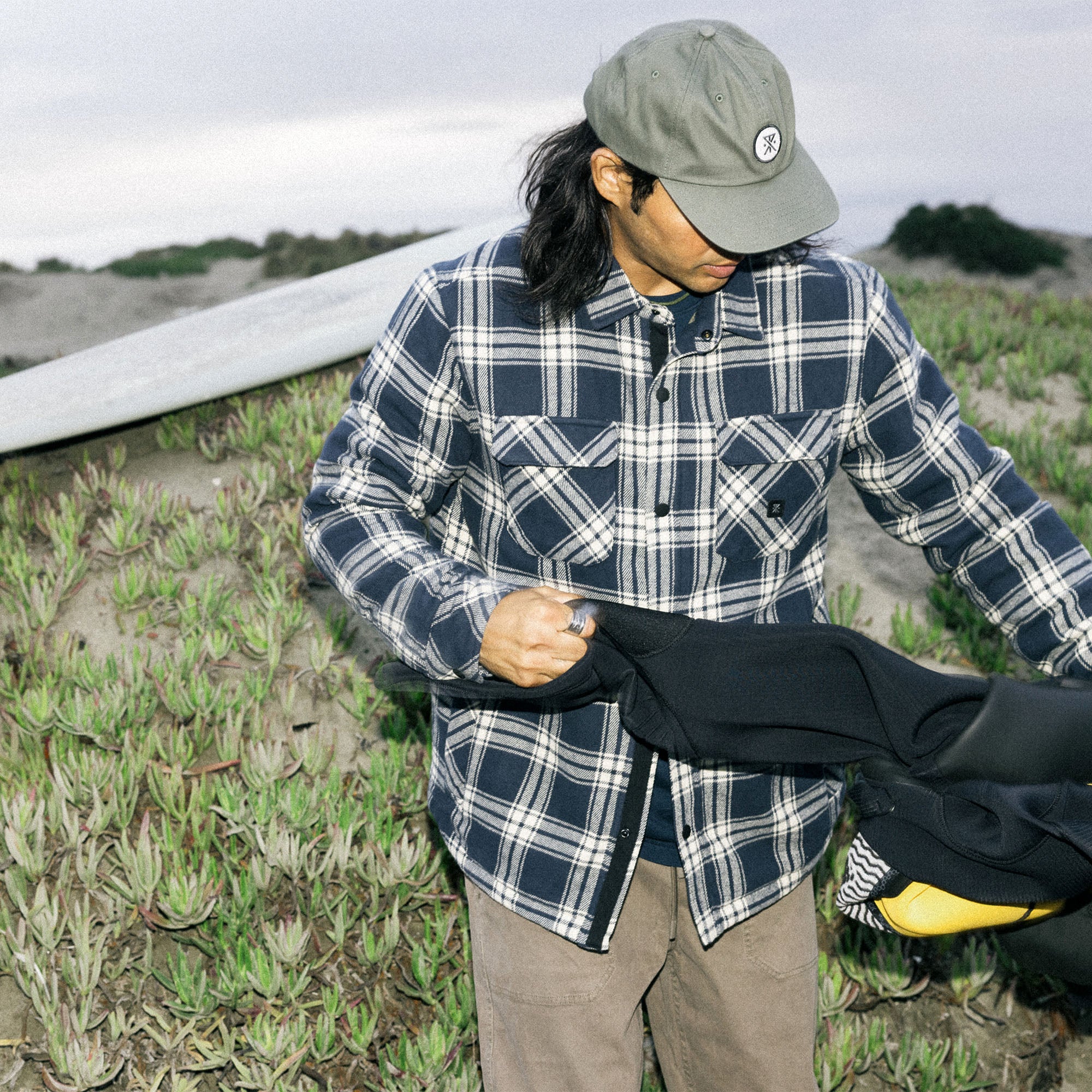 Man in a rugged Backwoods Overshirt Jacket with plaid flannel design, featuring denim accents and a cap, embodies outdoor adventure style.