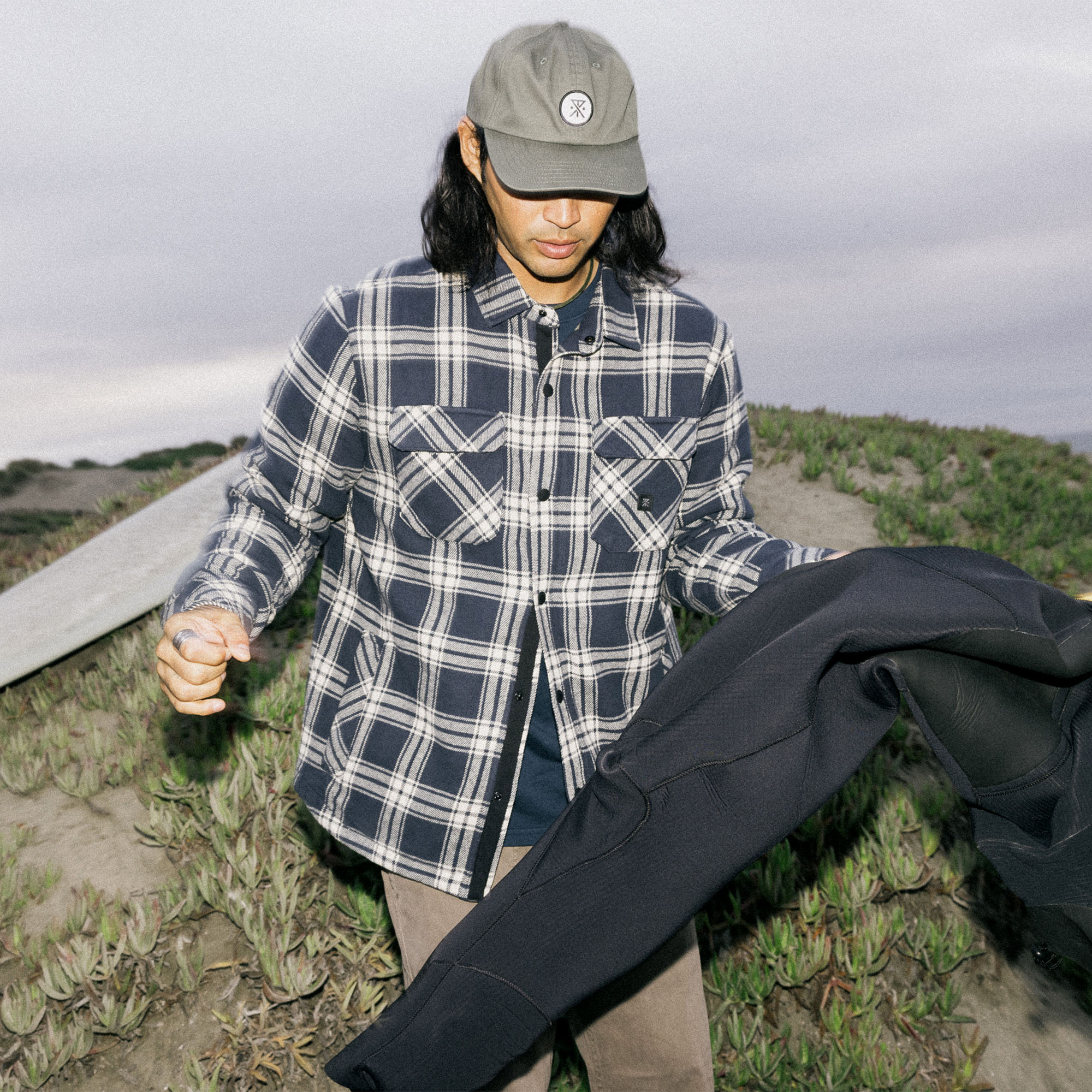 Man wearing a Roark Backwoods Overshirt Jacket in a flannel tartan pattern, styled with denim, ideal for outdoor adventures and travel.