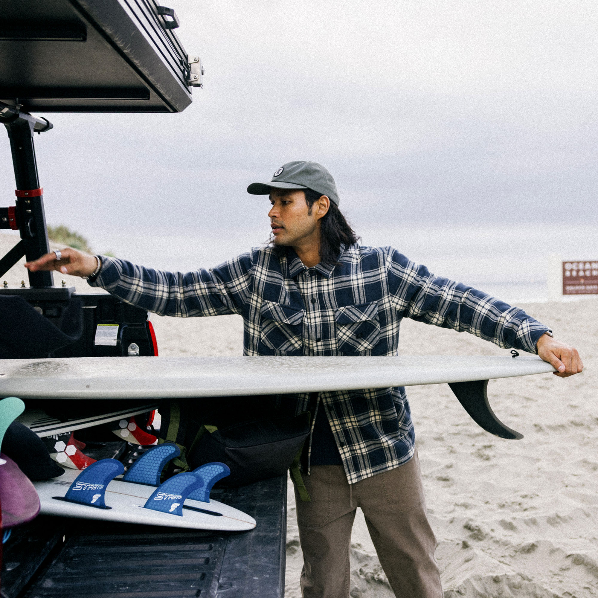 Surfboard leaning against a flannel overshirt jacket in a rustic outdoor setting, embodying Roark's spirit of adventure and boardsport lifestyle.