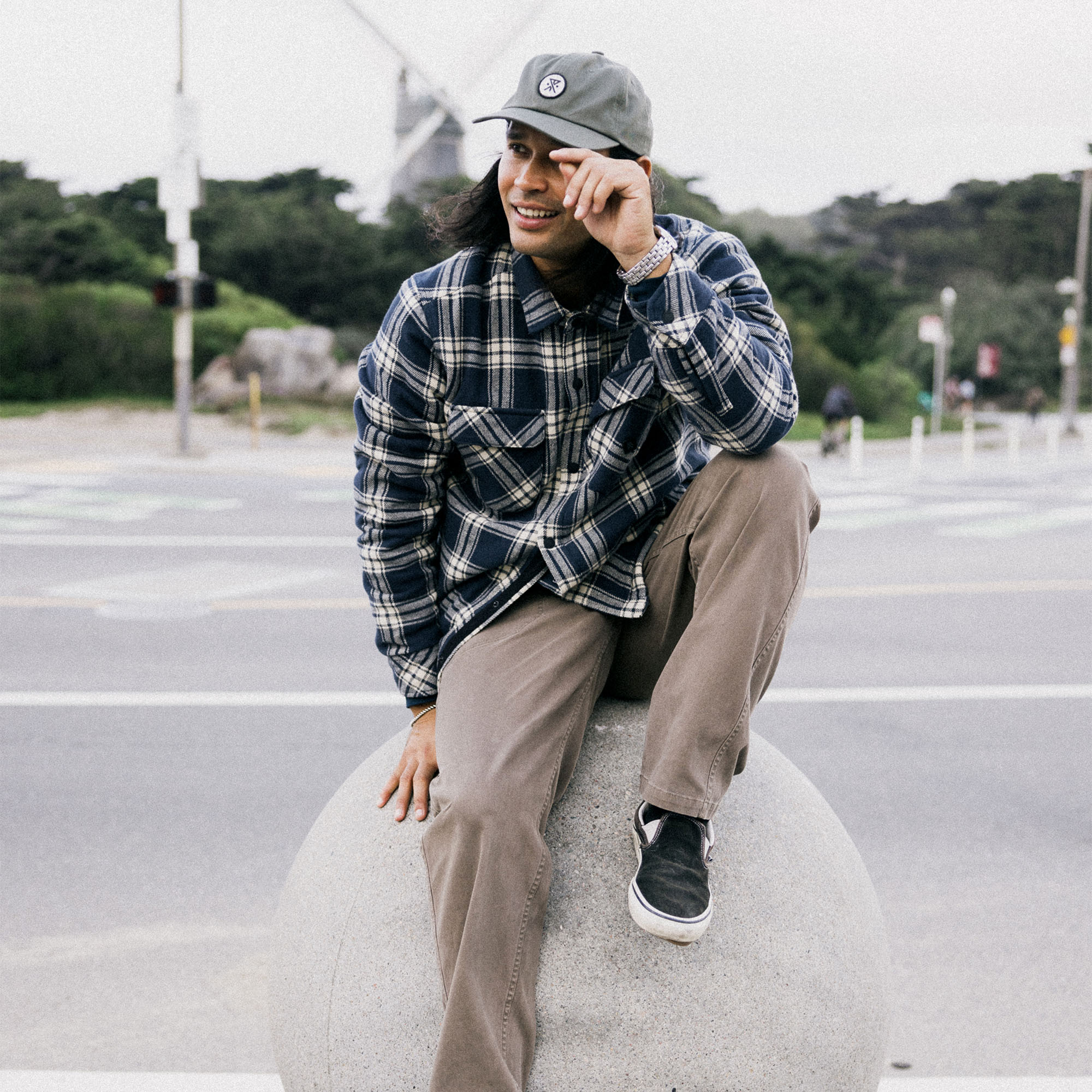 Man enjoying outdoor leisure in a flannel Backwoods Overshirt Jacket with a stylish cap, blending perfectly with a rugged, adventurous setting.
