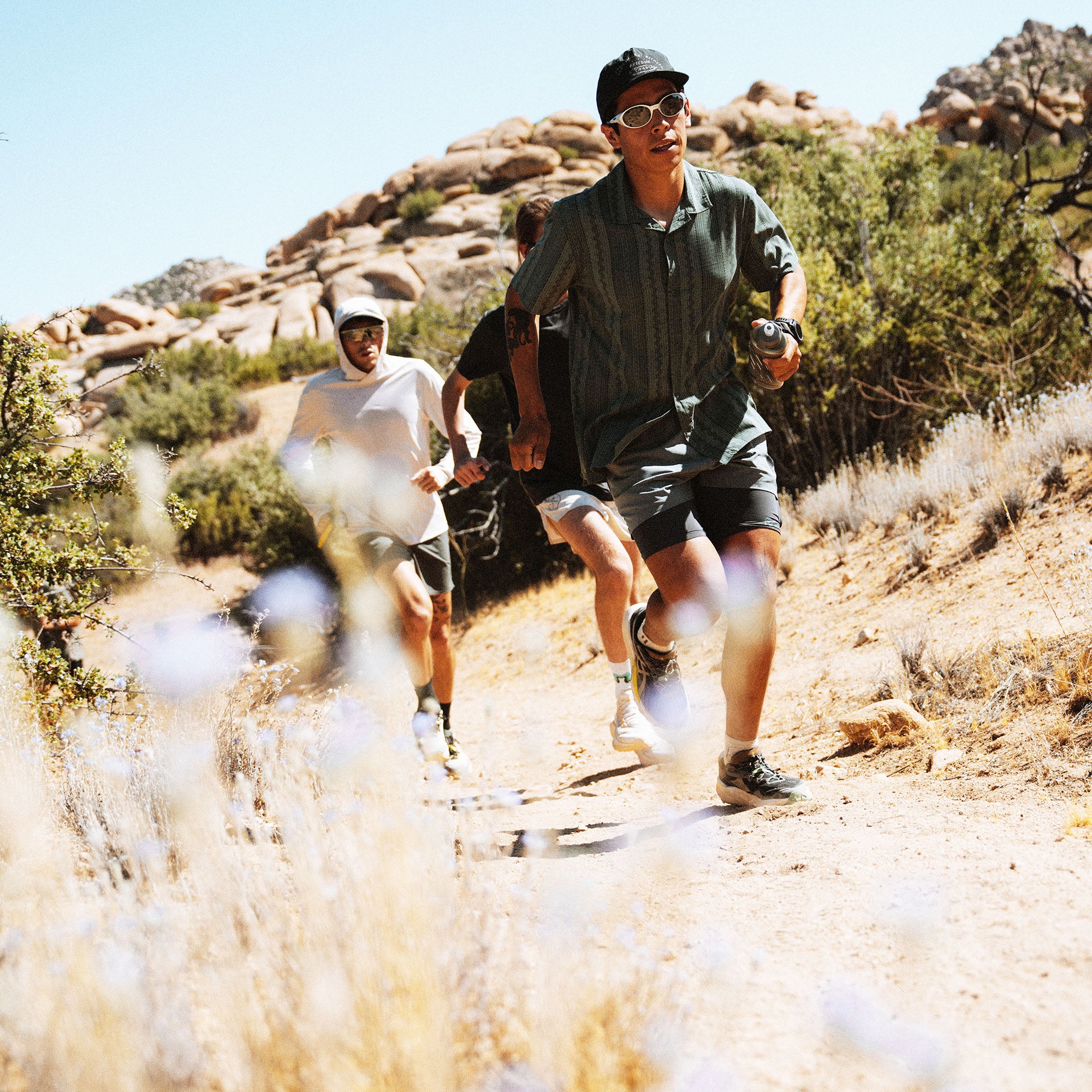 Three people trail running on a desert path with large rocks and desert vegetation in the background