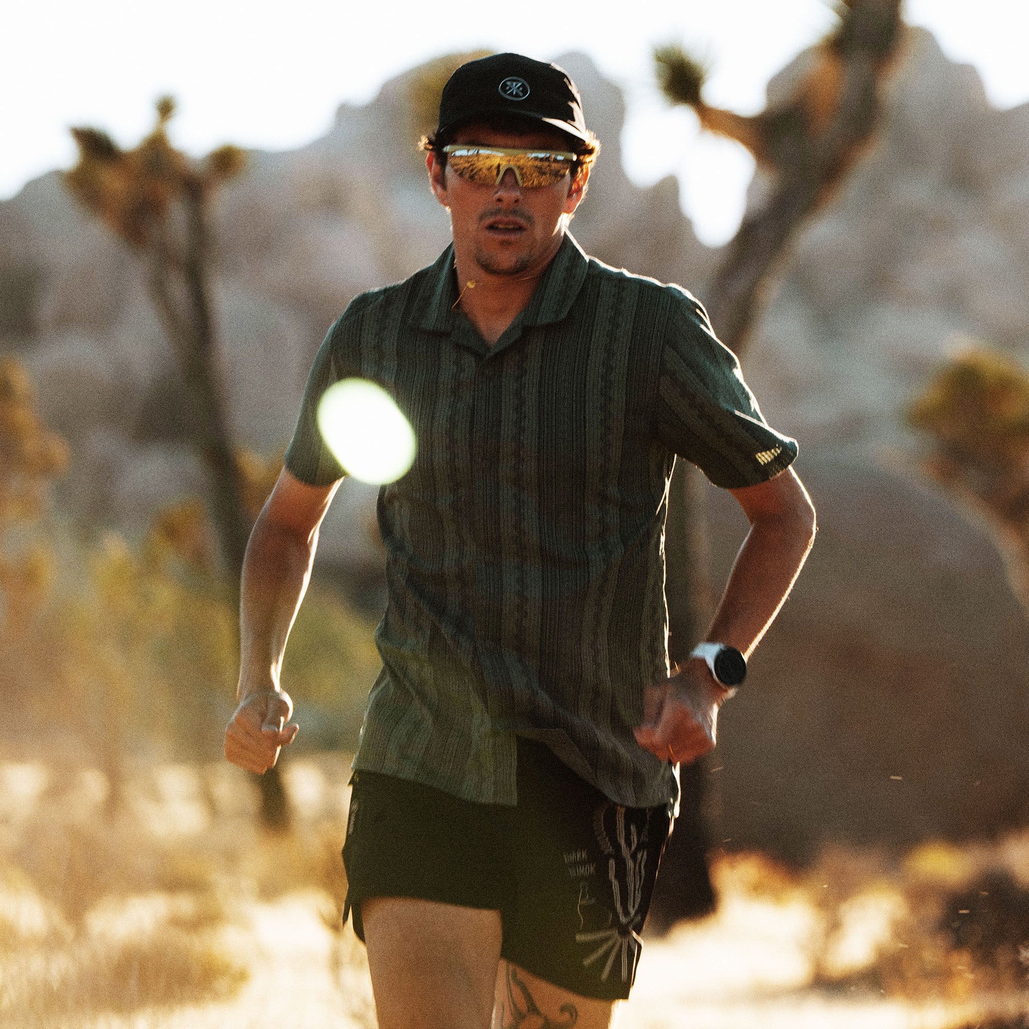 Man wearing sage green striped short-sleeve button-up shirt while trail running in desert landscape with Joshua trees