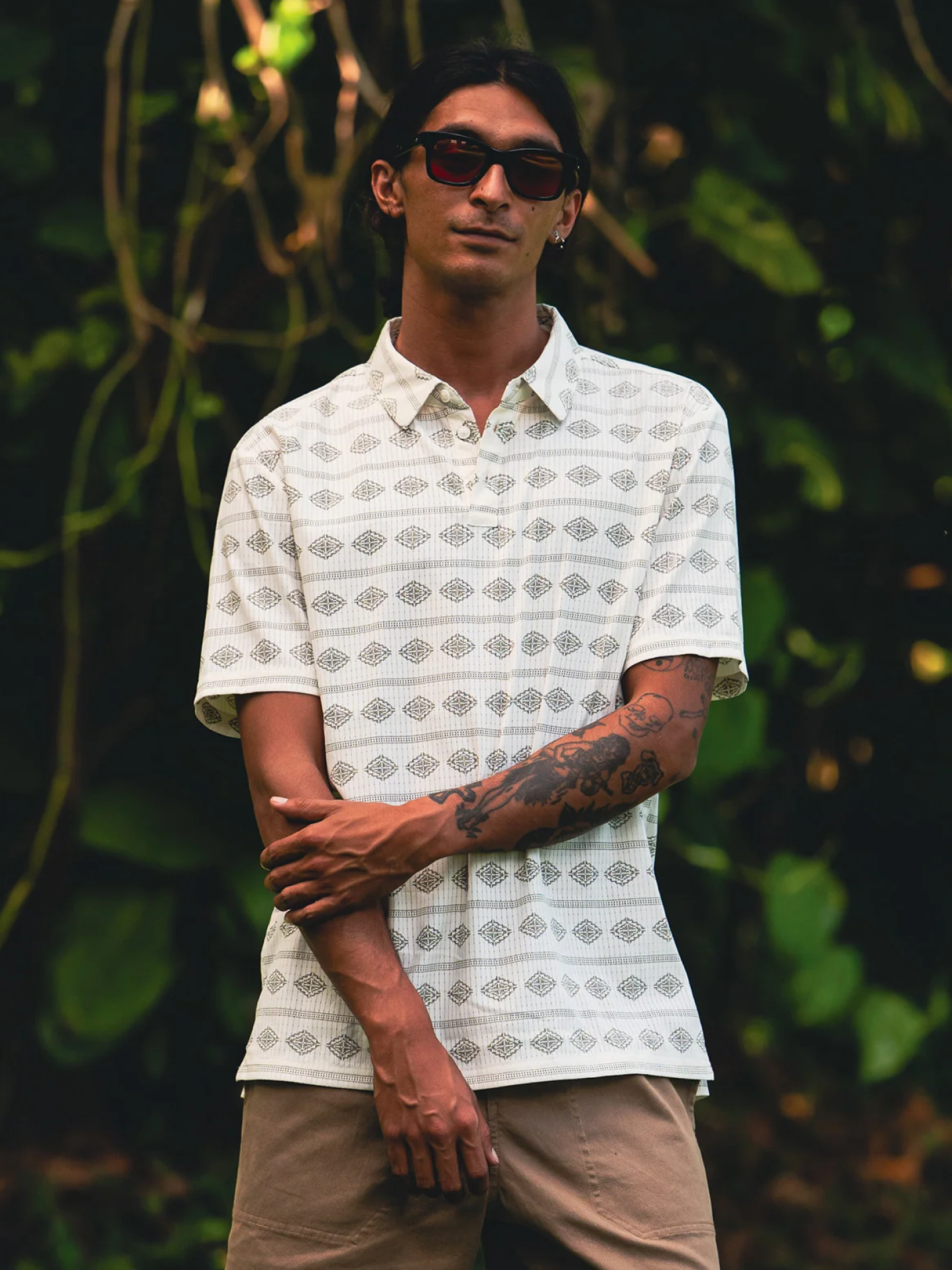 White geometric patterned polo shirt with collar, worn with khaki pants and dark sunglasses outdoors