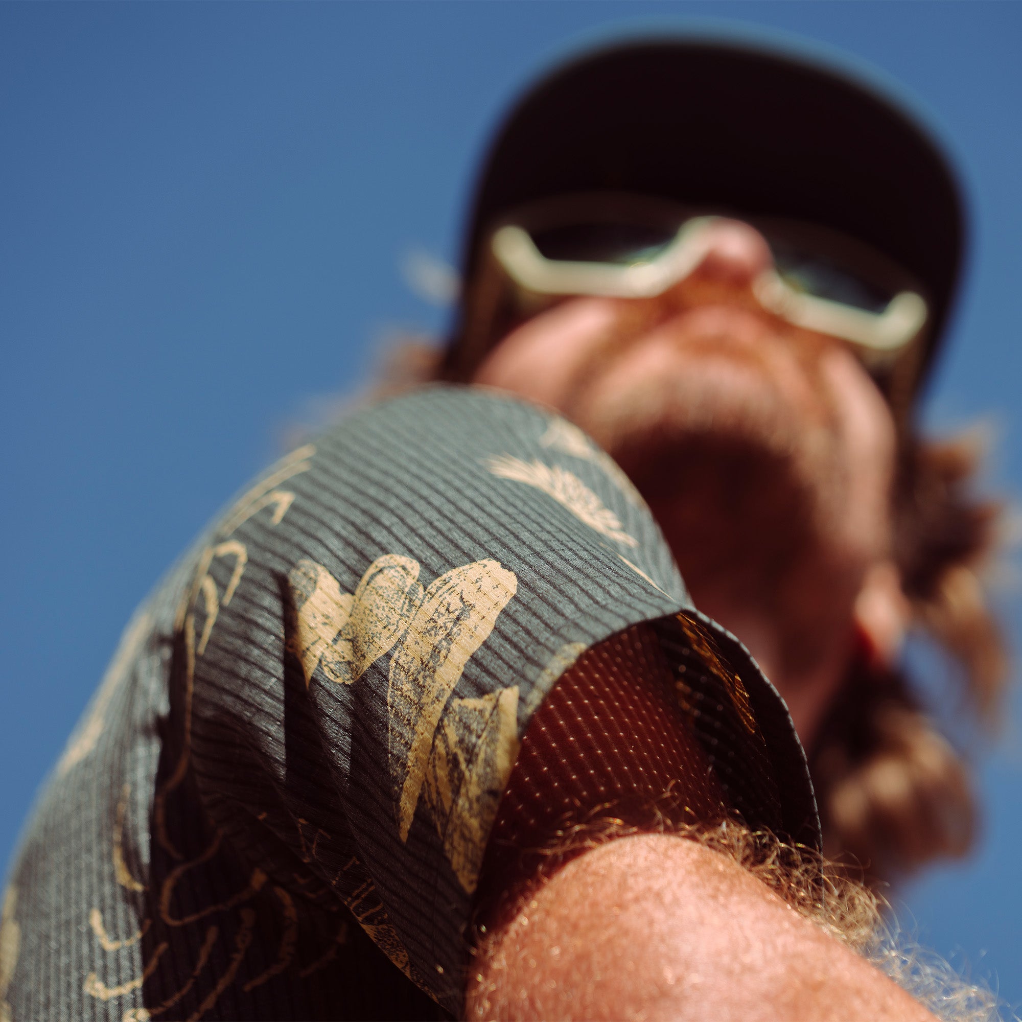 Adventurous individual wearing sunglasses, baseball cap, and sporting tattoos, exuding a carefree and rugged outdoor style for the Bless Up Trail.