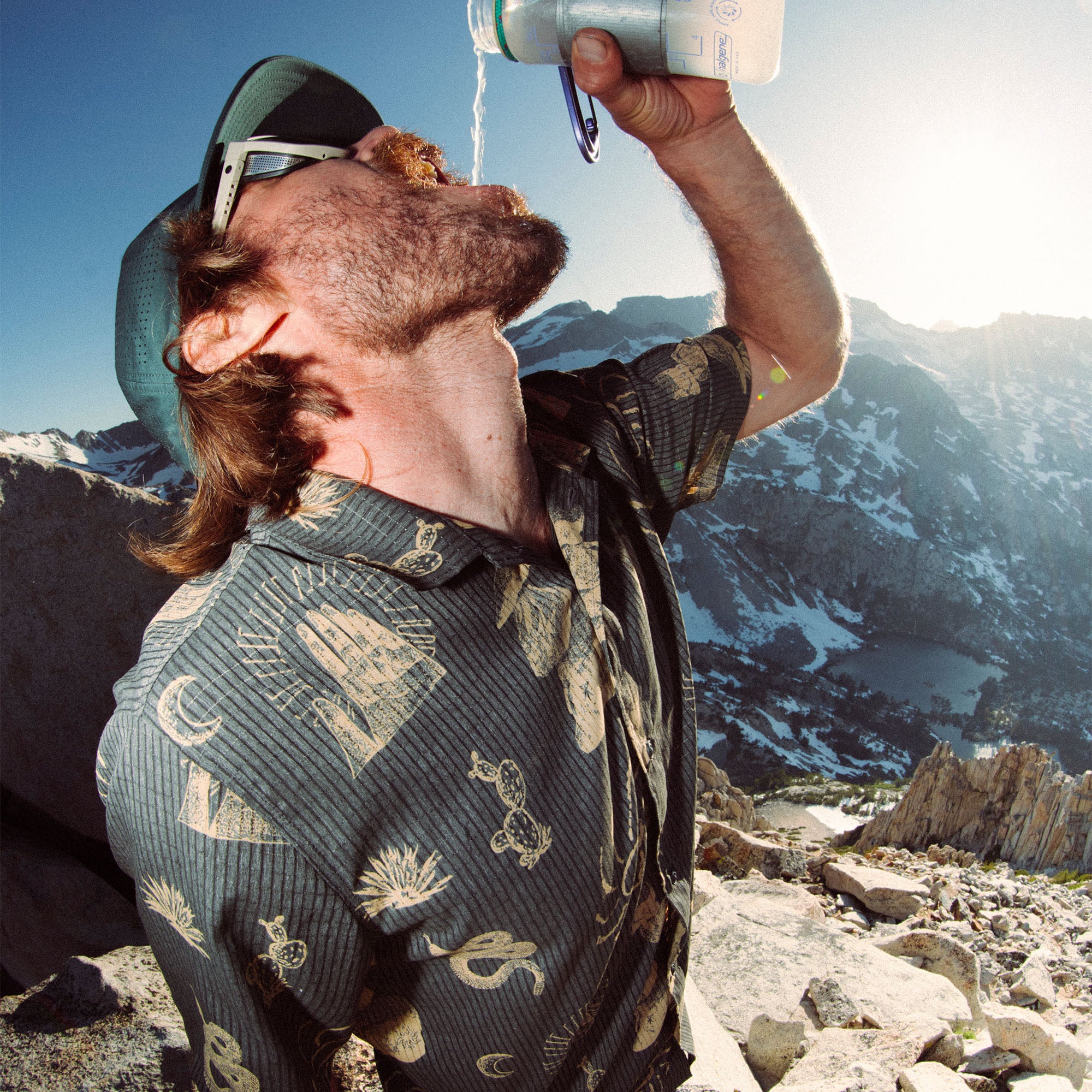 Man with a beard wearing a cap, drinking water during a vacation hike, embodying Roark's spirit of adventure and travel.