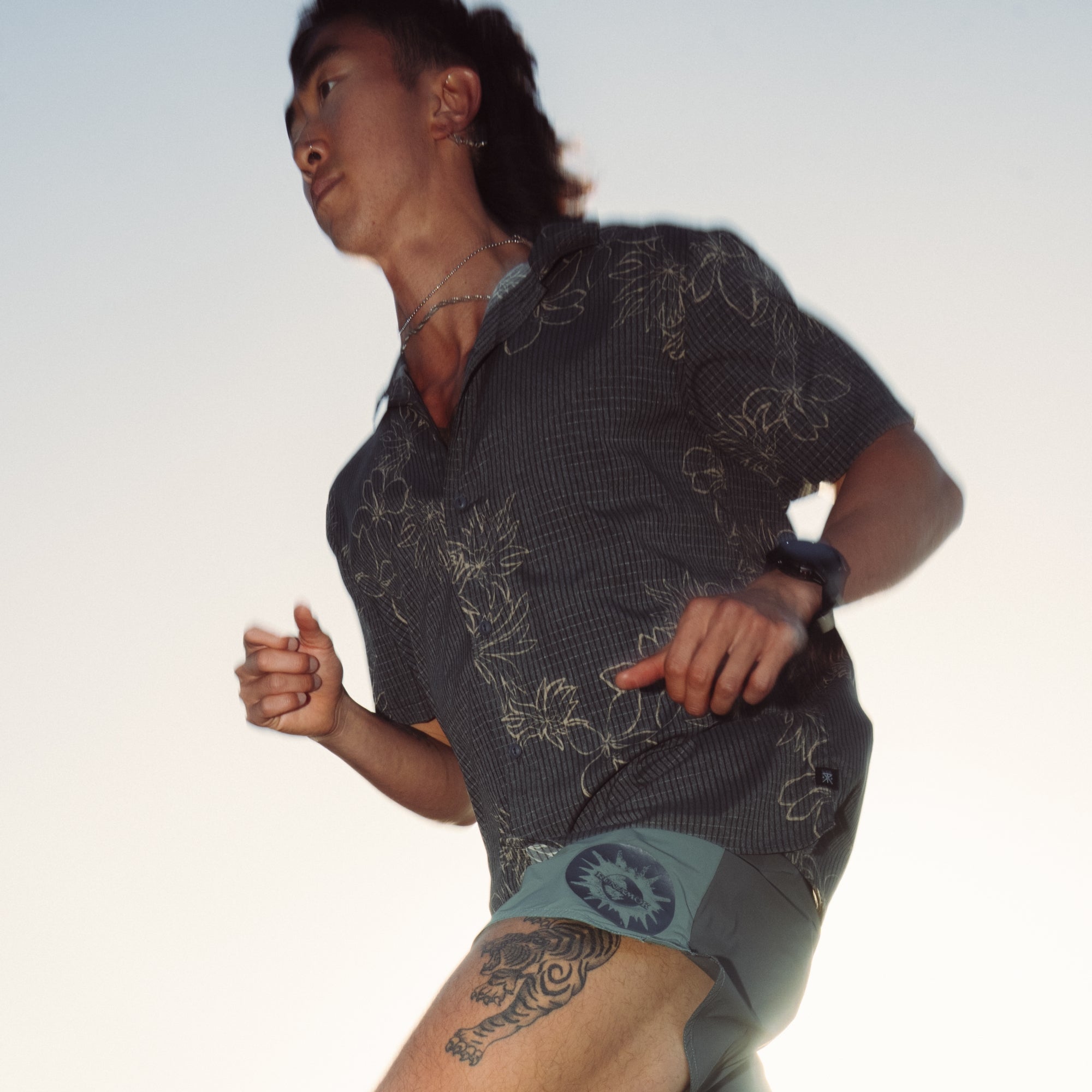 Man wearing camouflaged active shorts with his hands clasped in a 'bless up' gesture while standing on a scenic trail, embodying Roark’s spirit of adventure and exploration.