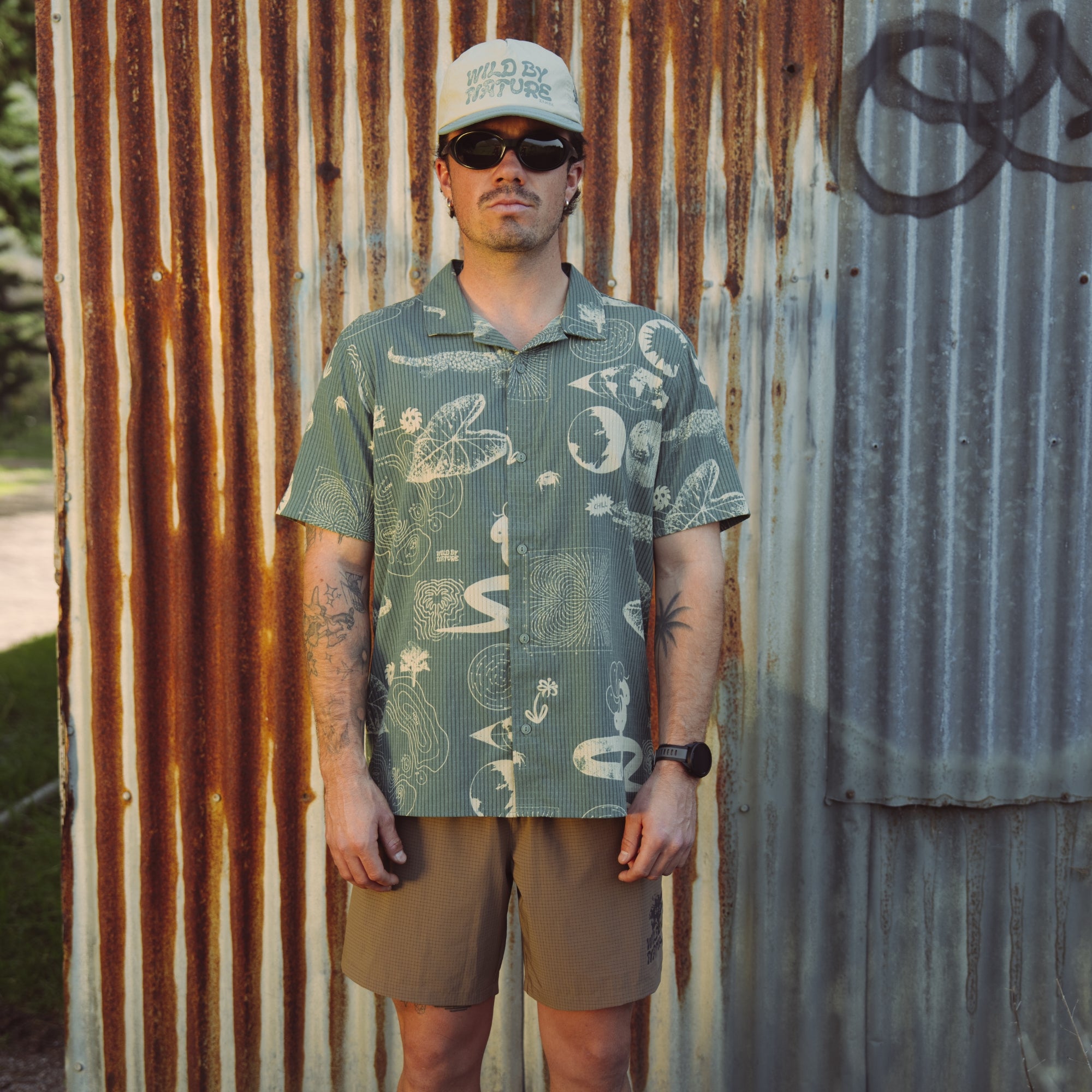 Adventurous man dressed in Roark's active shirt and Bermuda boardshorts, ready for a trail exploration, featuring prominent buttons and sleek sleeves.