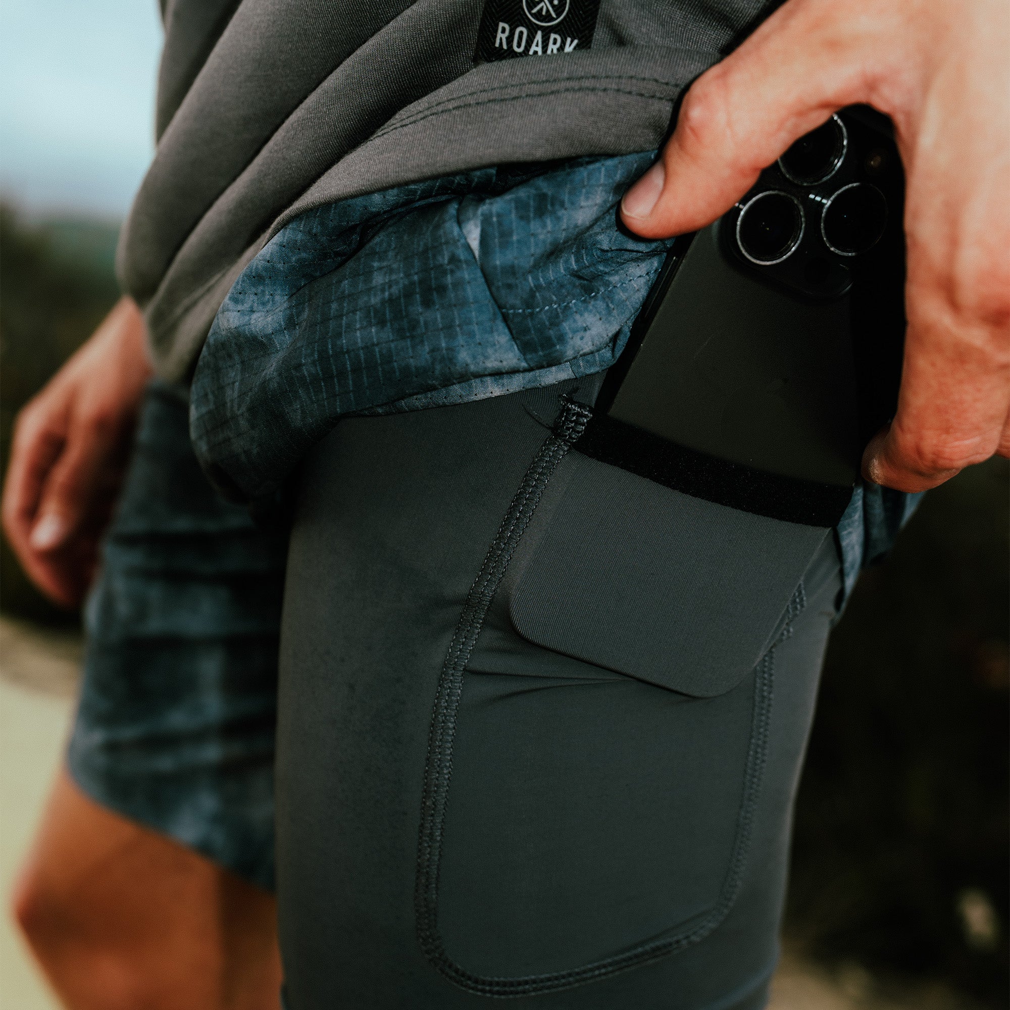 Person wearing charcoal Roark shorts with teal patterned inner lining and secure pocket for phone storage
