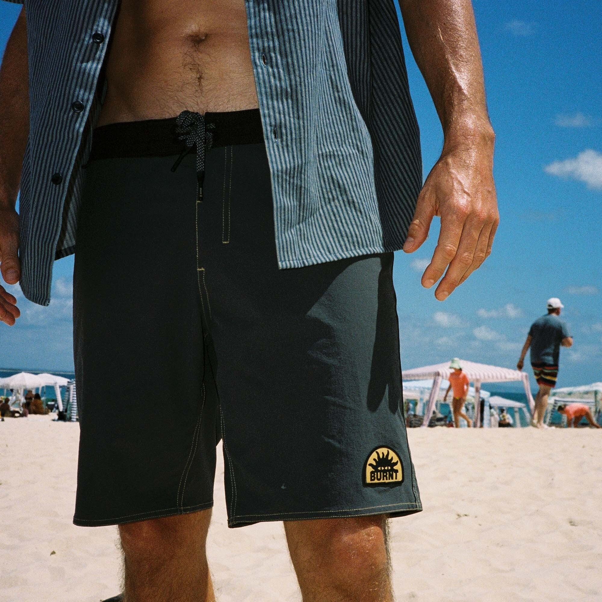 Assorted Roark Burnt Collection boardshorts and active shorts displayed on a scenic beach, emphasizing adventure and outdoor lifestyle.