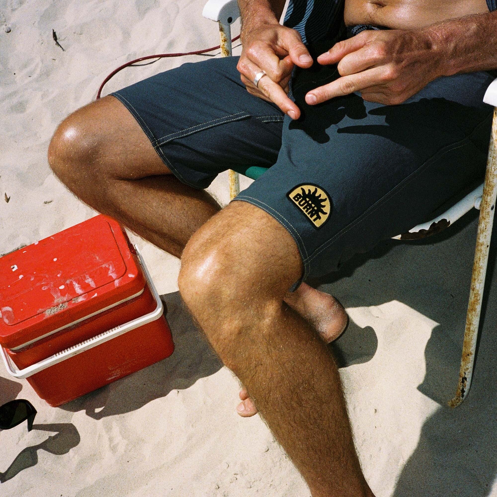 Assorted Roark Burnt Collection summer shorts displayed on a scenic beach setting, including boardshorts, active shorts, and Bermuda trunks for adventure travel.