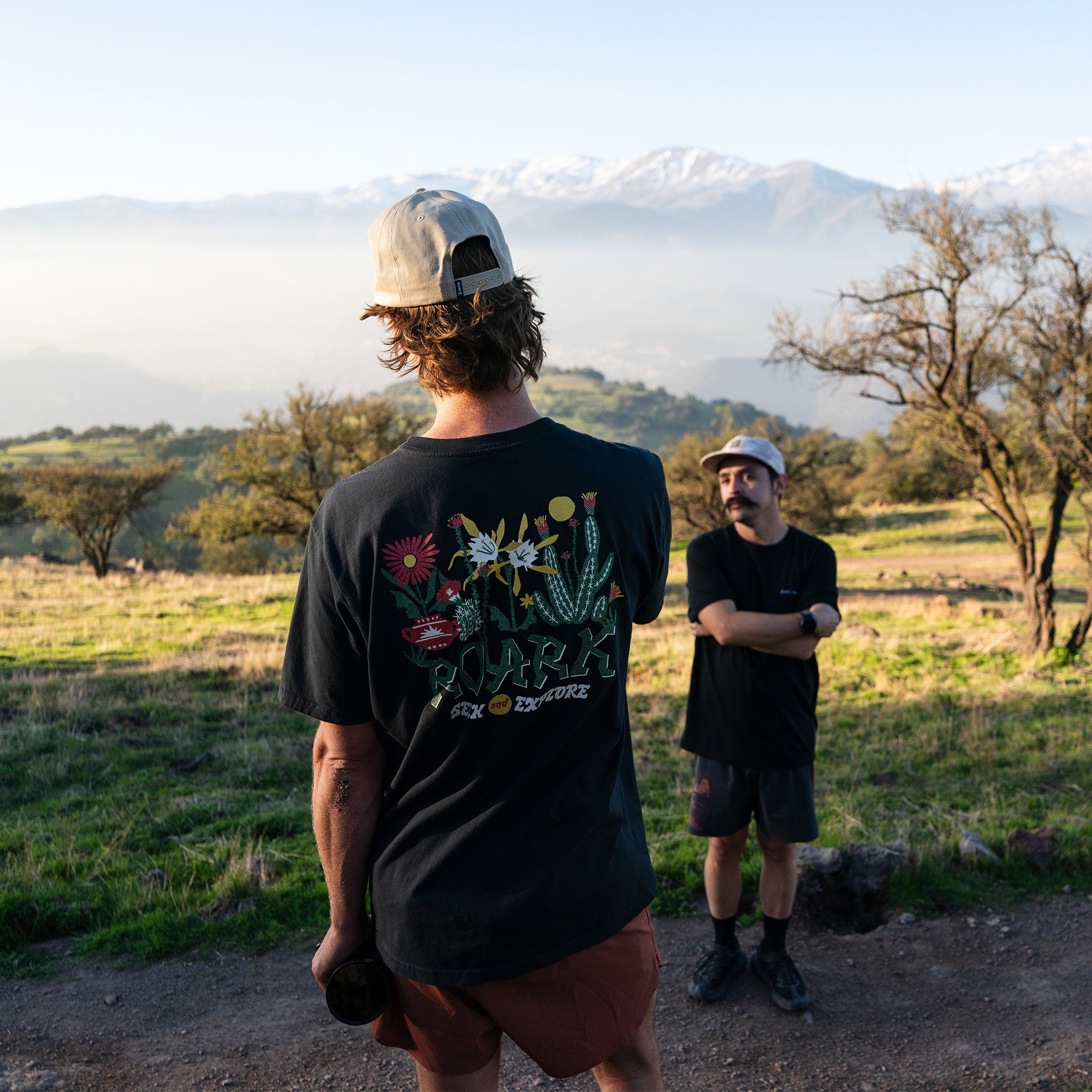 Group of adventurous people wearing casual outdoor attire including caps and fedoras, gathered in a scenic cactus garden, showcasing the spirit of exploration and nature.