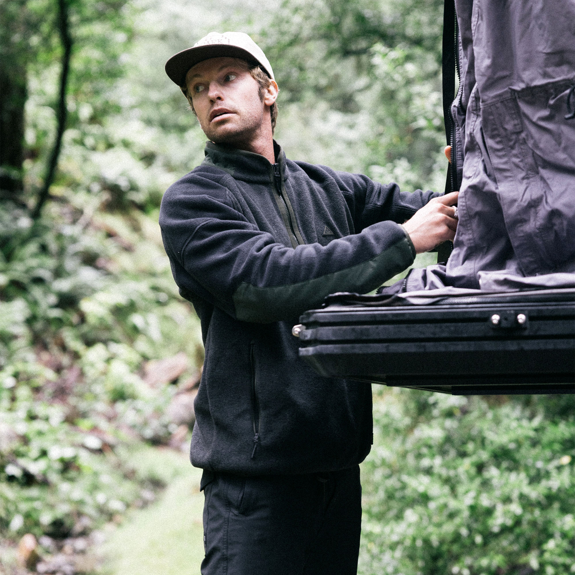 Man wearing a cozy Campover Fleece Mock Hoodie with a beanie, exploring a snowy winter landscape, reflecting Roark's commitment to adventure and outdoor apparel.