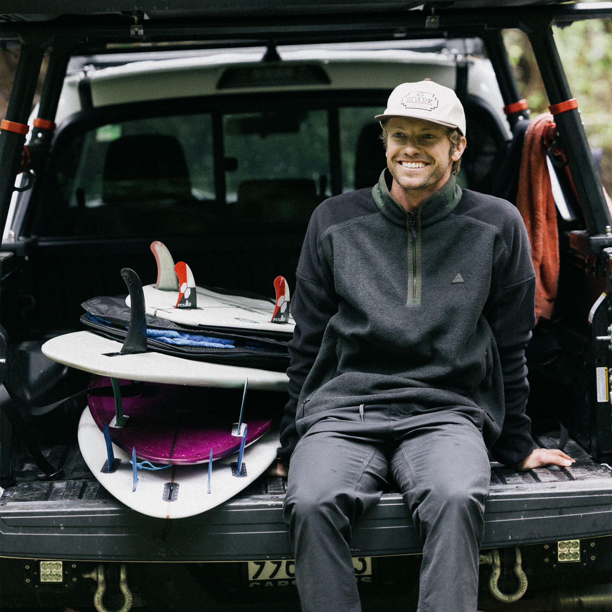 Happy adventurer wearing a baseball cap and a cozy Campover Fleece Mock Hoodie from Roark's HO25 collection, smiling outdoors