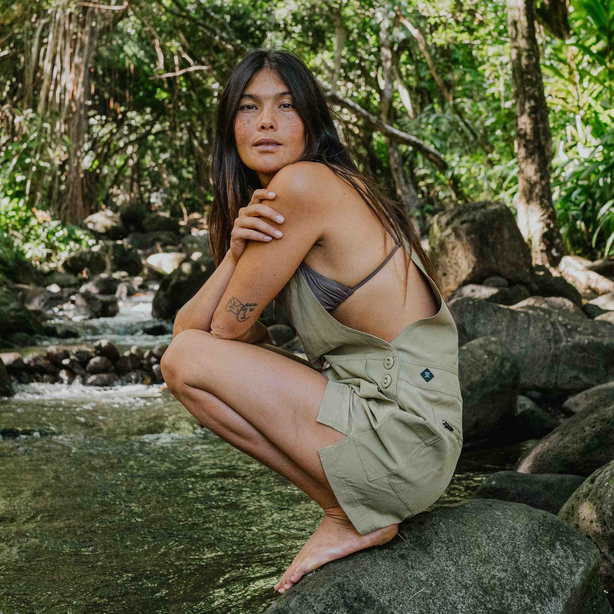 Model wearing a sleeveless Canyon Romper by Roark, perfect for vacation, showcasing a relaxed fit and adventurous style with visible foot detail on rugged terrain.
