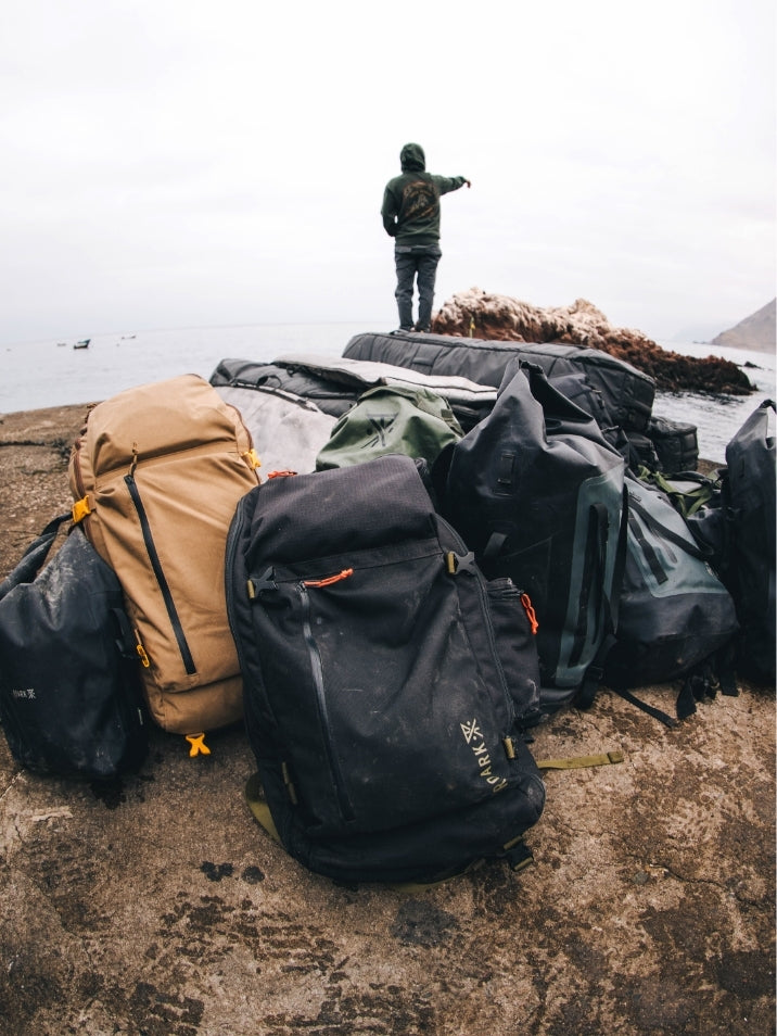 Adventure-ready travel accessories laid out on bedrock, showcasing a durable Roark bag, ideal for outdoor and recreation activities.