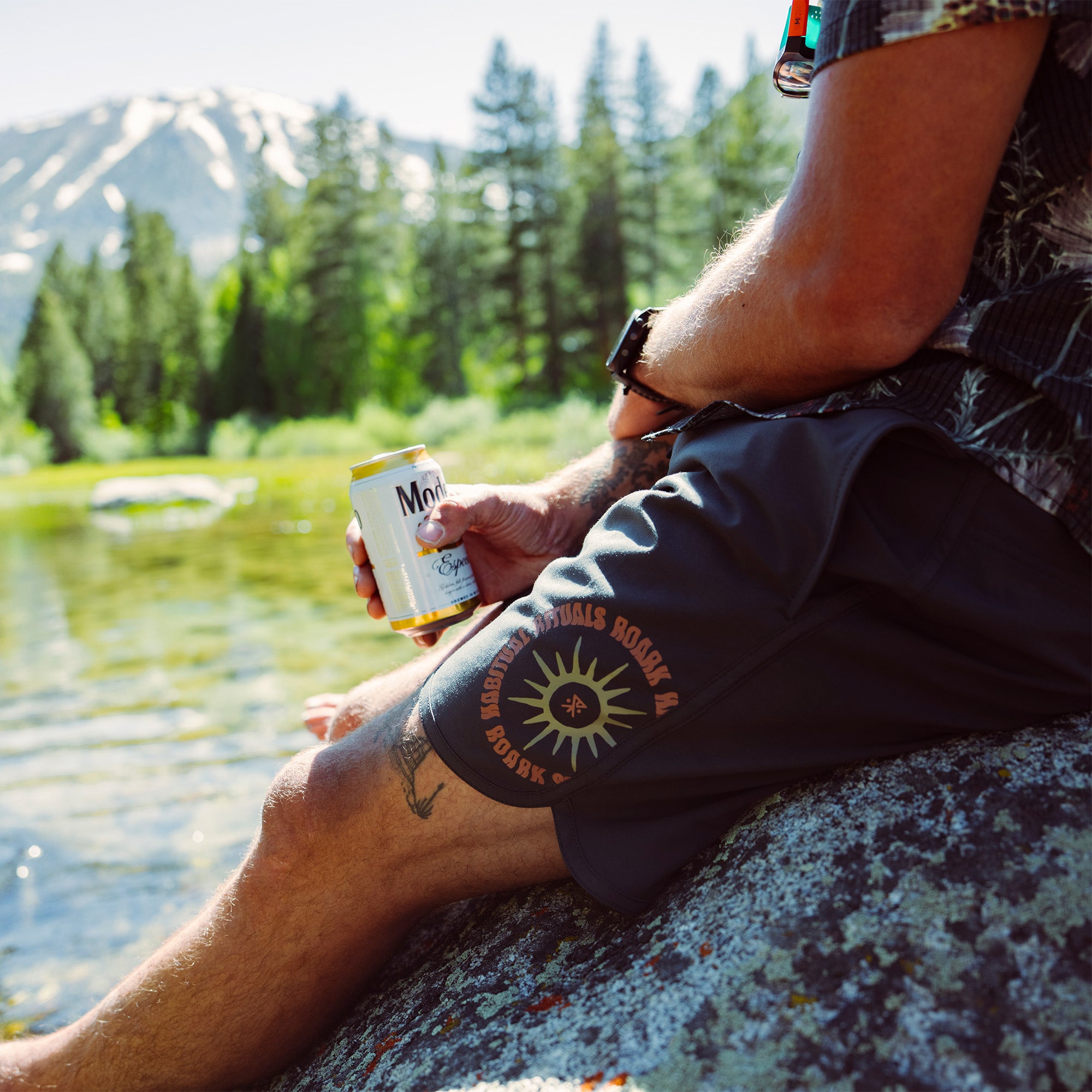 Person refreshes with a cold drink in a scenic outdoor setting, embodying the adventurous spirit ideal for Roark Chiller Boardshorts.