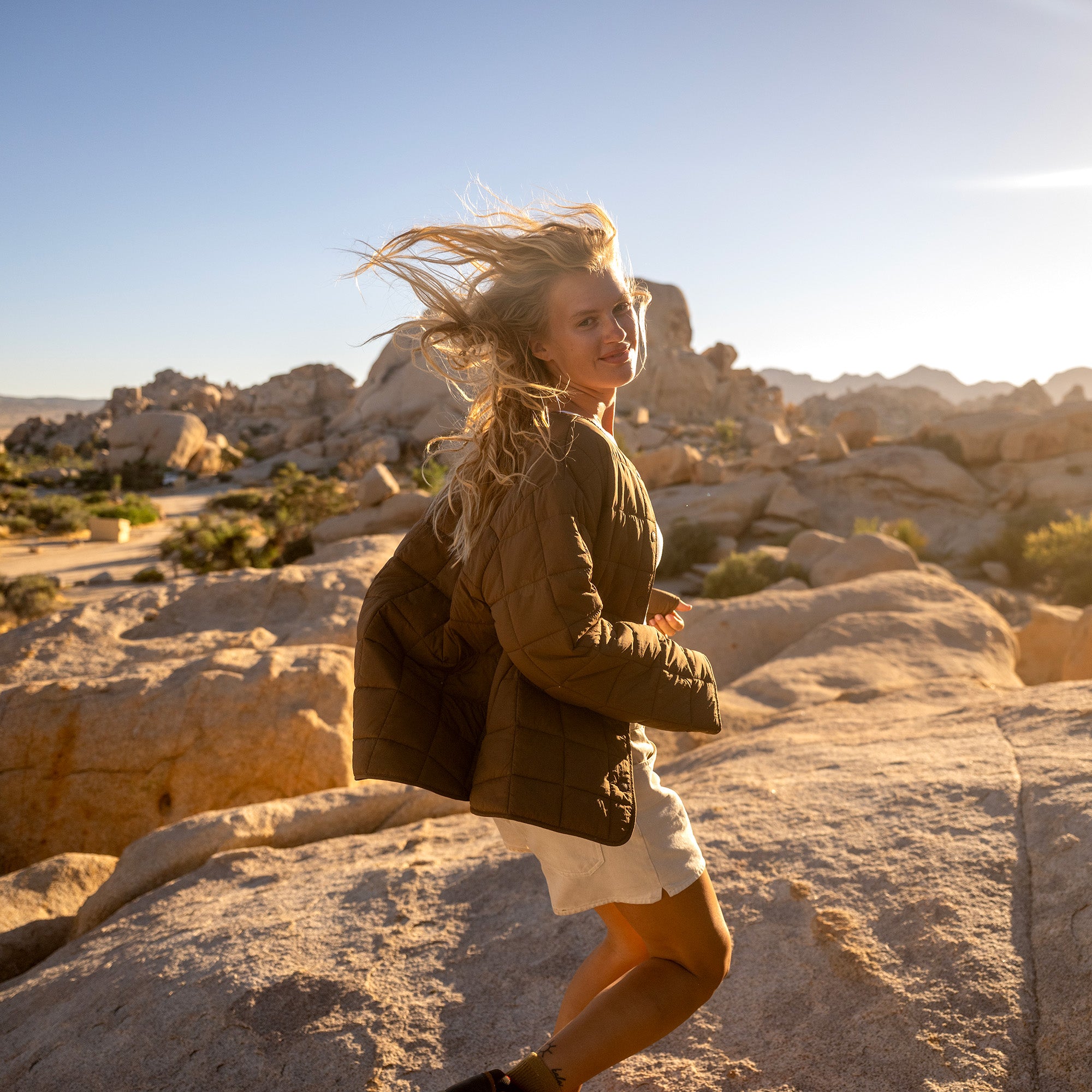 Woman jogging in black quilted jacket on rocky desert terrain with boulders in background