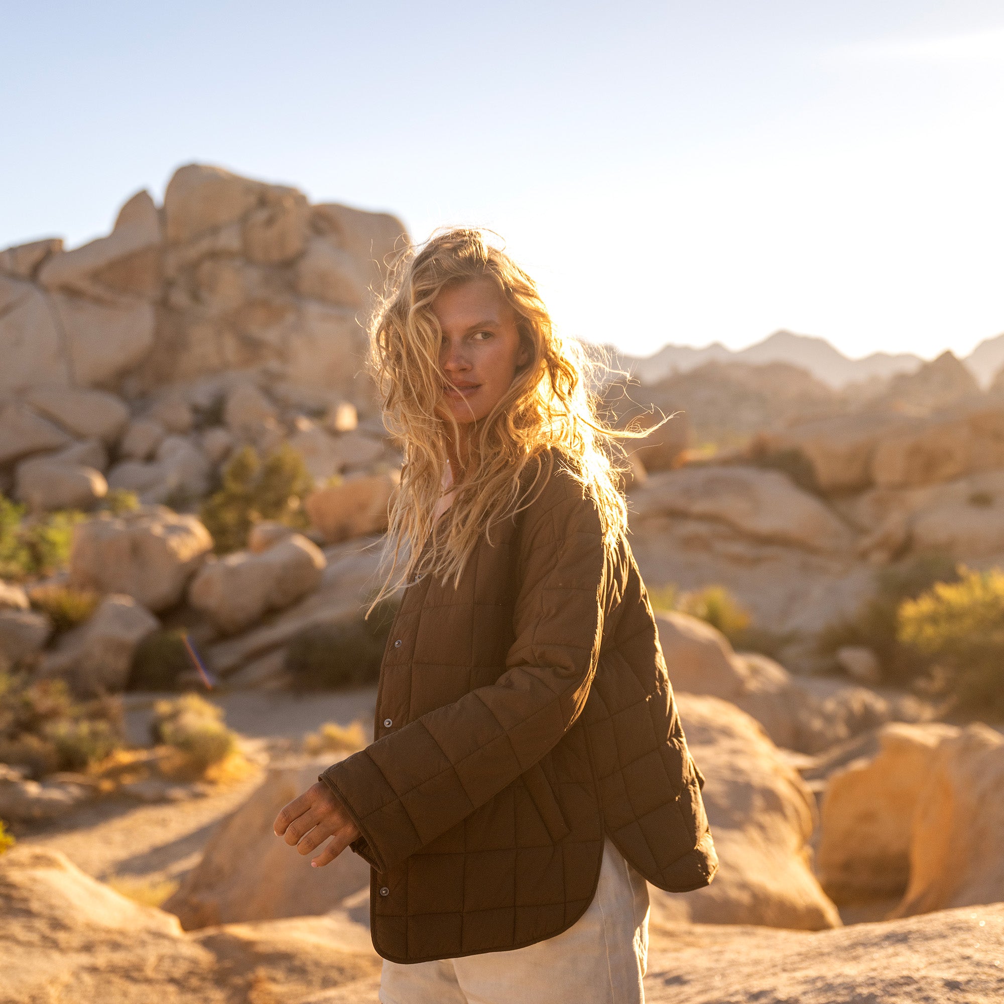 Woman wearing black quilted Cloud Liner Jacket in desert landscape with large boulders and golden hour sunlight