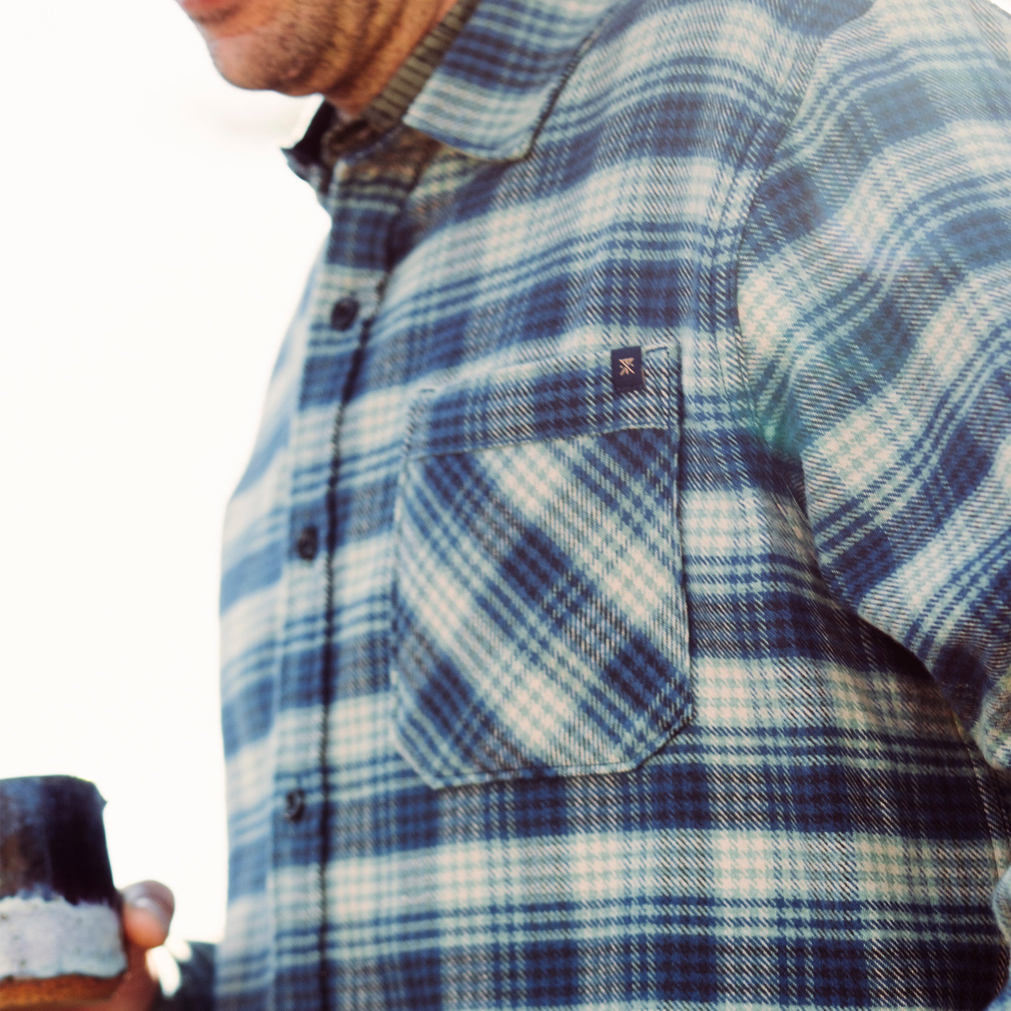 Blue and tartan plaid Crossroads organic cotton flannel draped over rubble, highlighting Roark's commitment to durable, adventure-ready apparel.