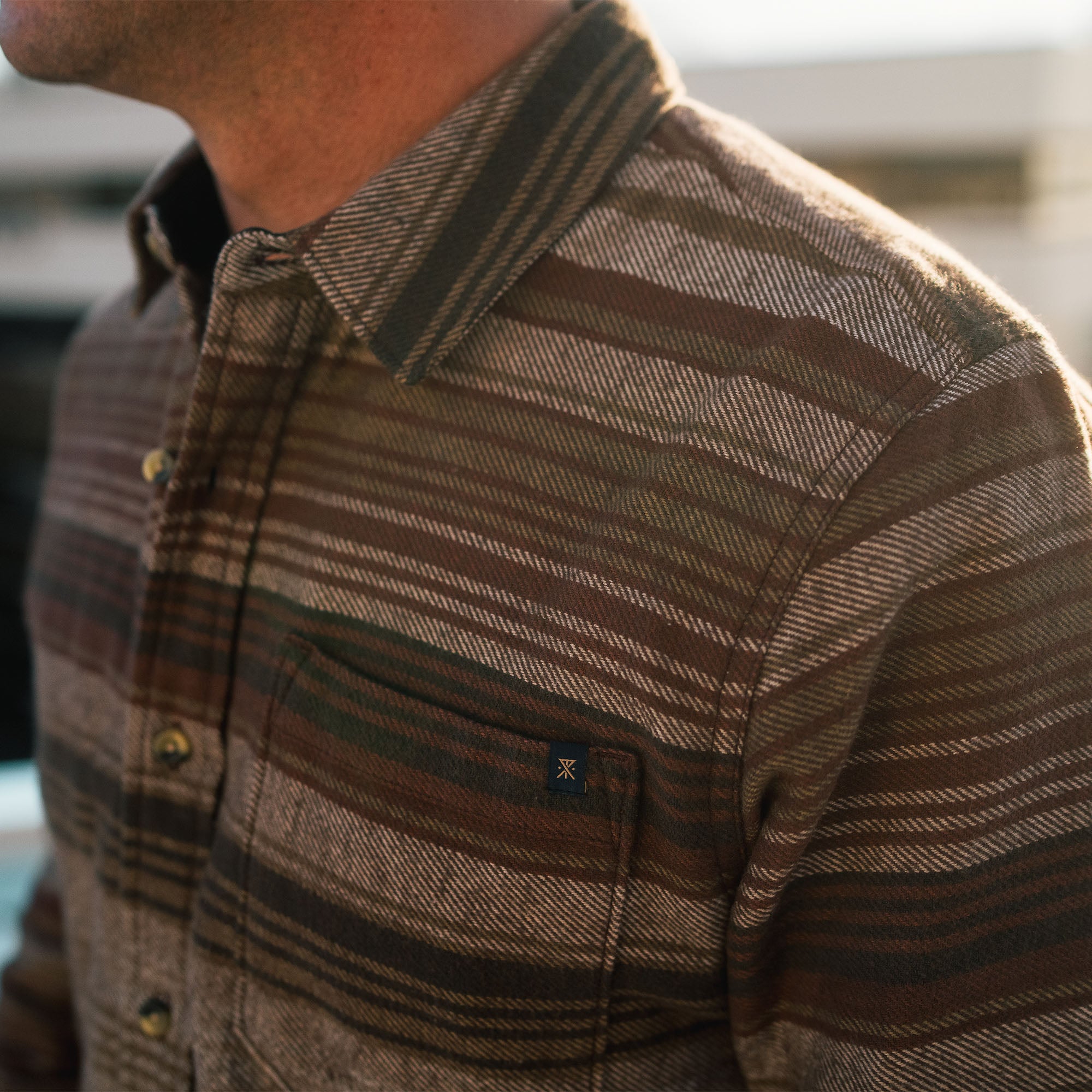 Brown organic cotton flannel shirt by Roark, ideal for adventure and travel, displayed at a scenic outdoor crossroads.
