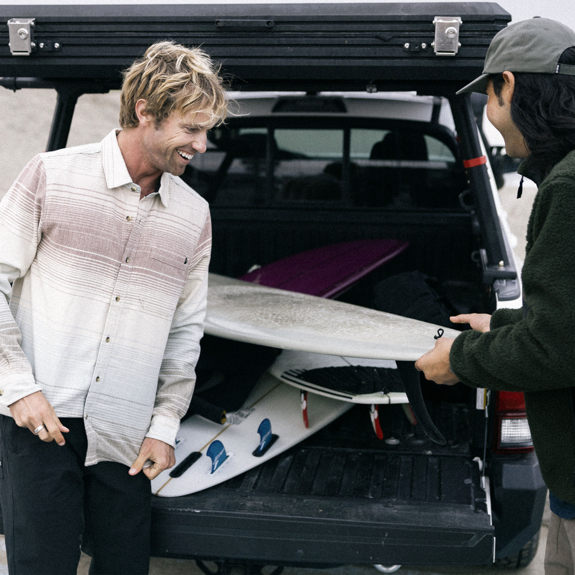 Surfer arranging surfboards at a beachside photo shoot, highlighting the style and versatility of Roark's Crossroads Organic Cotton Flannel.