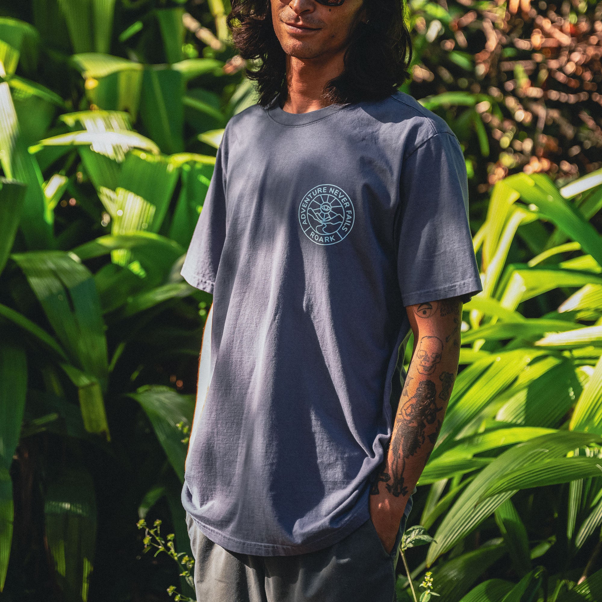 Stylish active shirt with sleeves, paired with denim, set against a backdrop of palm trees, capturing Roark's adventurous and outdoor spirit.