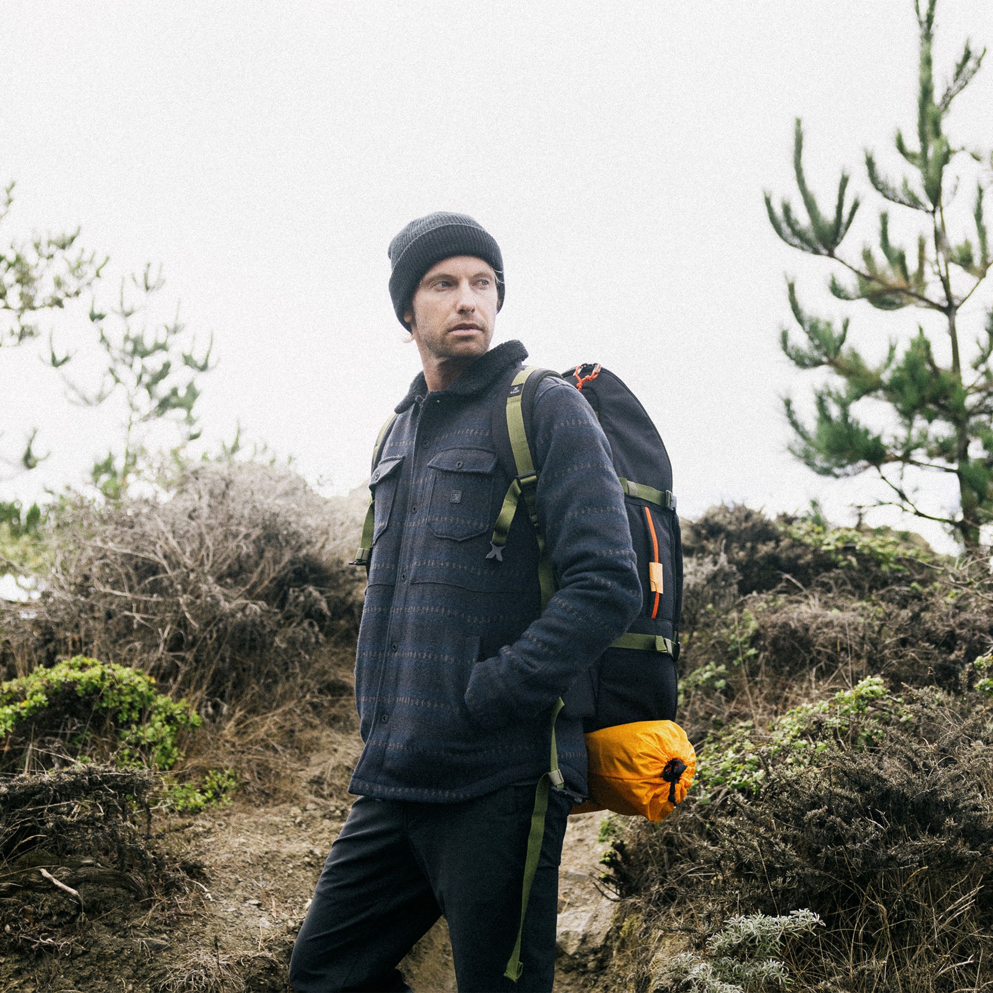 Adventure traveler in rugged outdoor setting wearing Roark's Hebrides Jacket, standing beside luggage and embracing the natural landscape.