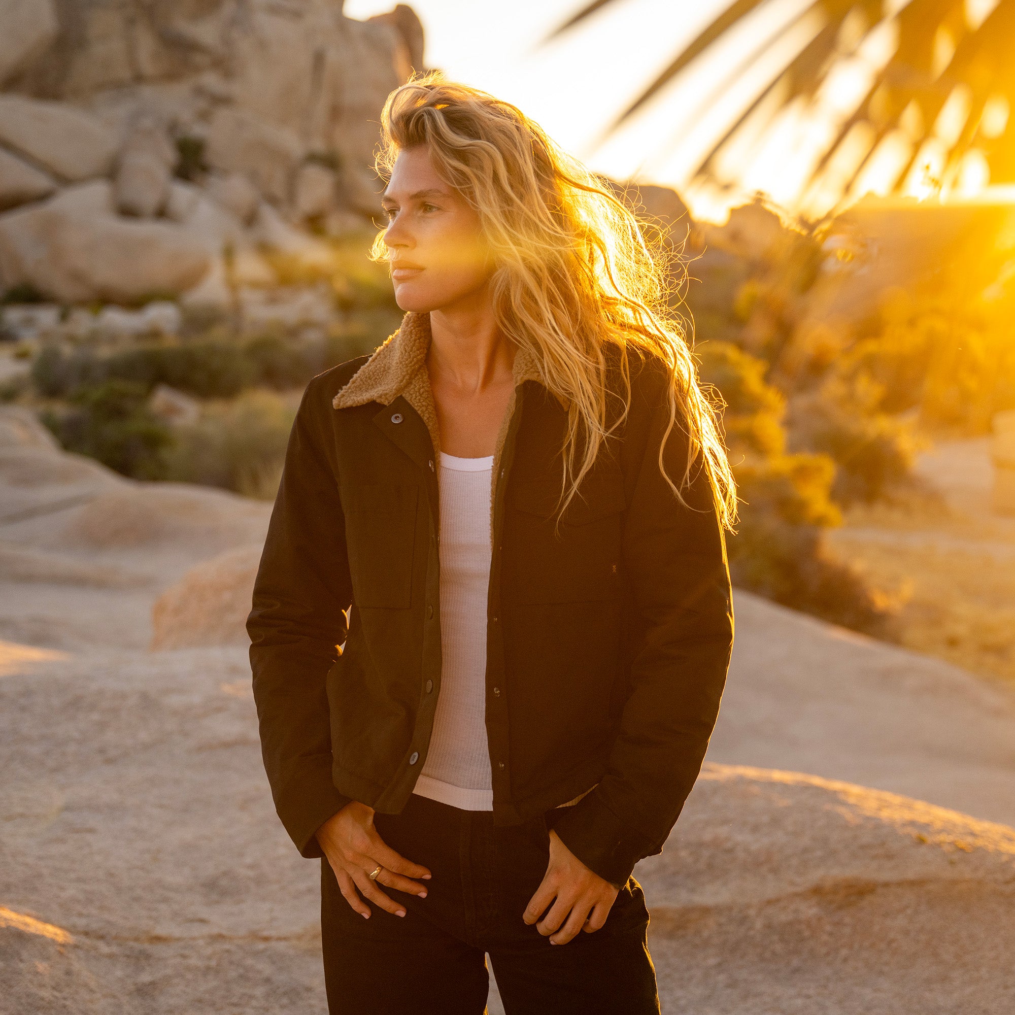Woman wearing black Hebrides Sherpa Jacket with white ribbed shirt at sunset in rocky desert landscape