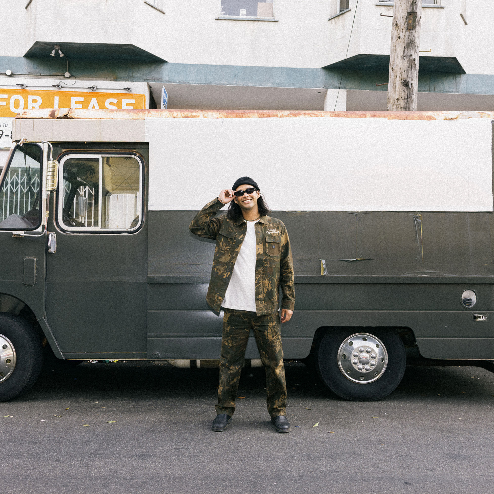 Model wearing Roark's adventure-ready Hebrides Unlined Jacket in a military camouflage pattern, styled with coordinating cargo pants, evoking a rugged, outdoor explorer look.