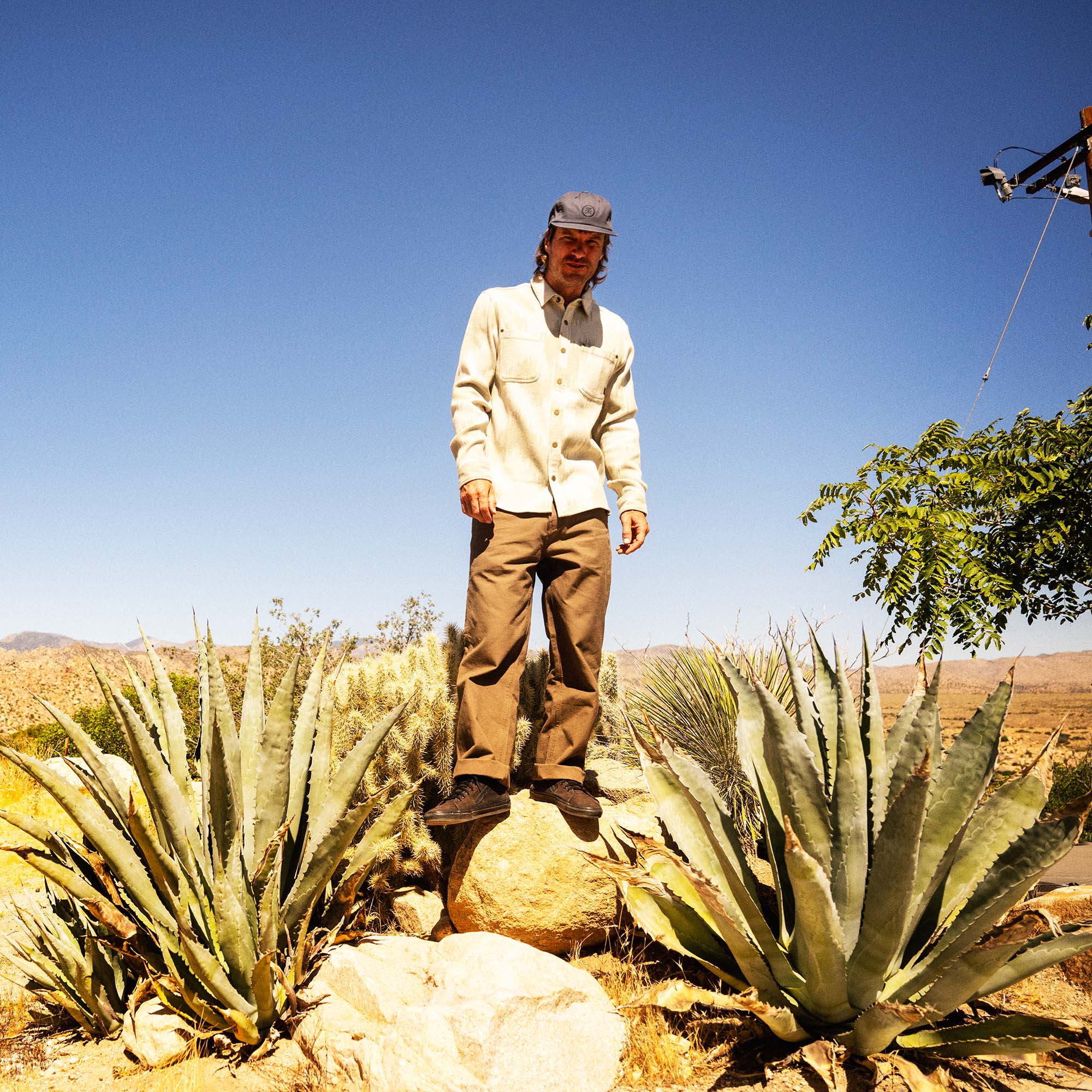 Man wearing cream Journey Jacquard long sleeve flannel shirt and tan pants standing in desert landscape surrounded by agave plants