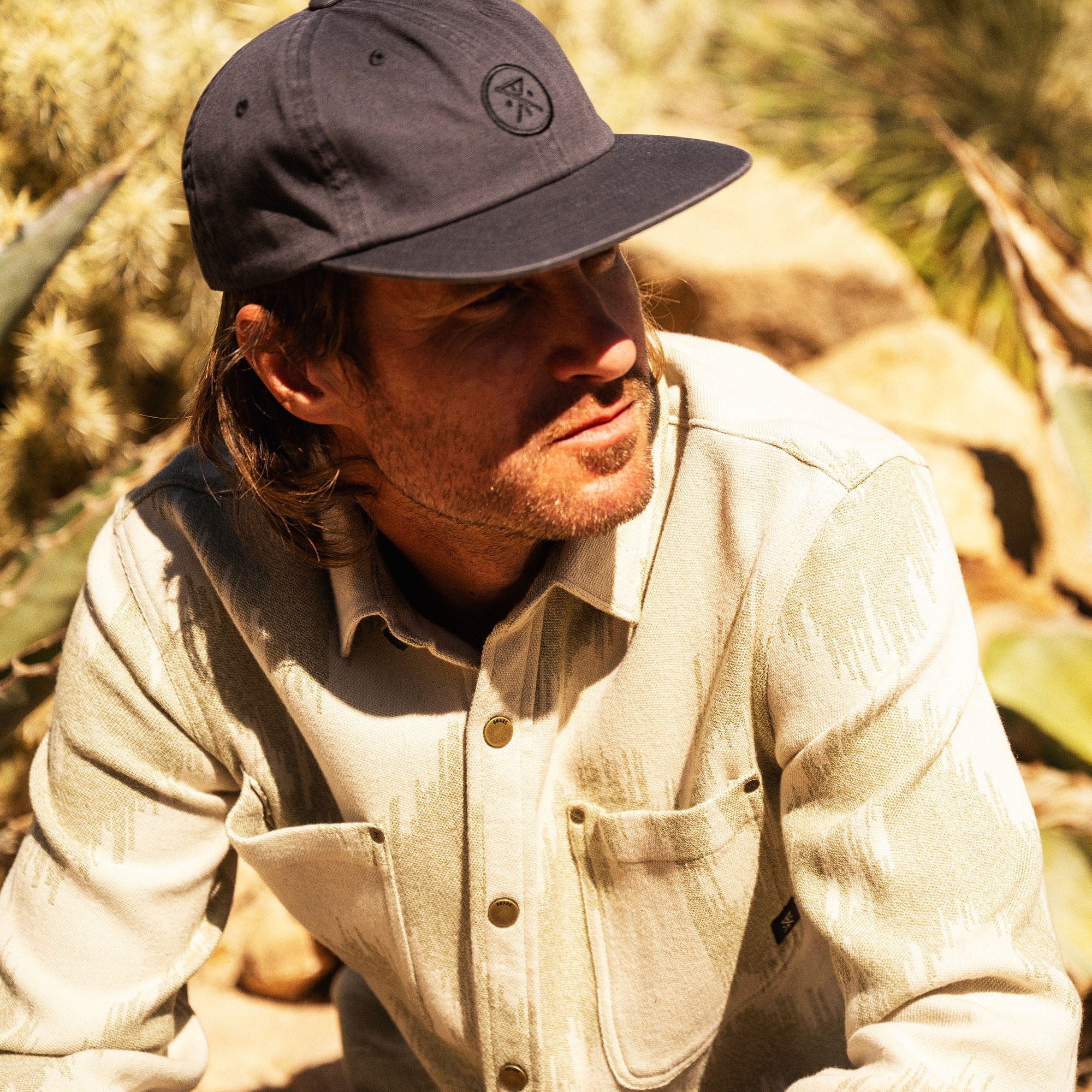 Man wearing charcoal snapback cap and cream long-sleeve flannel shirt outdoors in natural sunlight