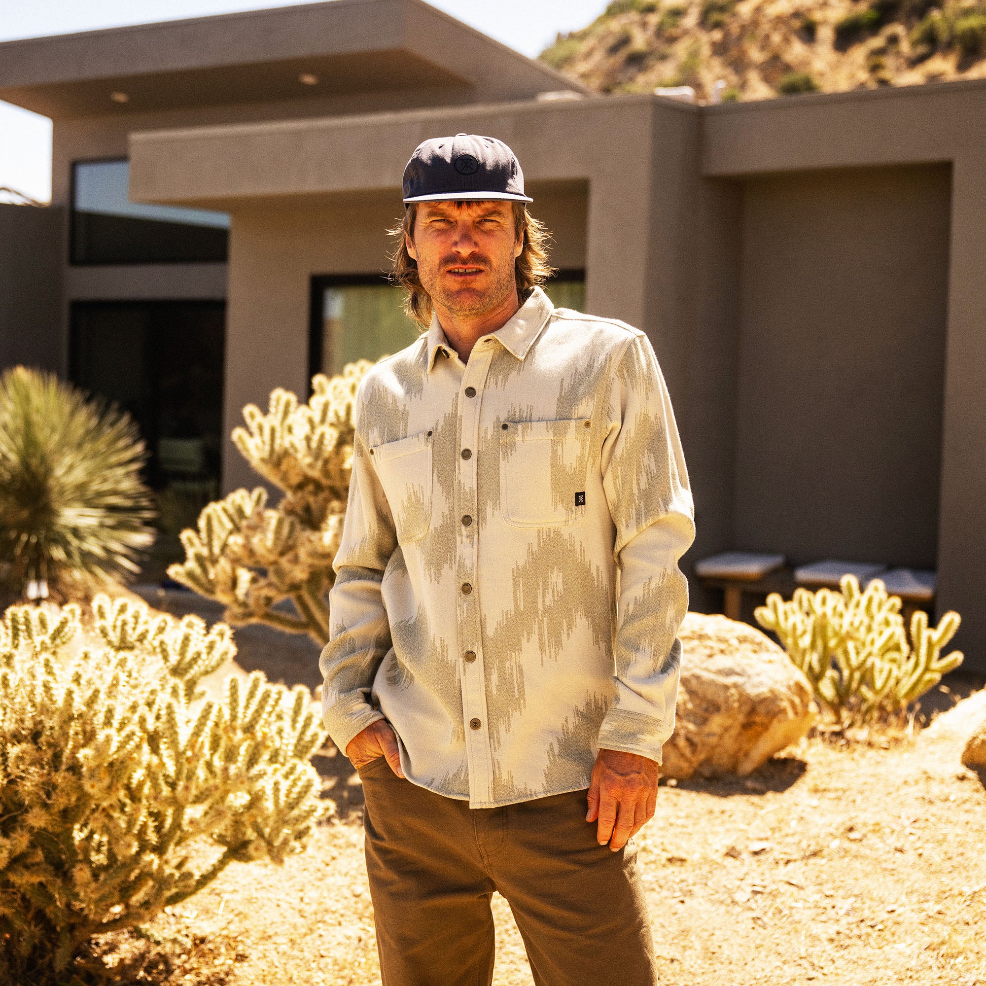 Oat Journey Jacquard long sleeve flannel shirt worn by man standing in desert landscape with cacti and modern building