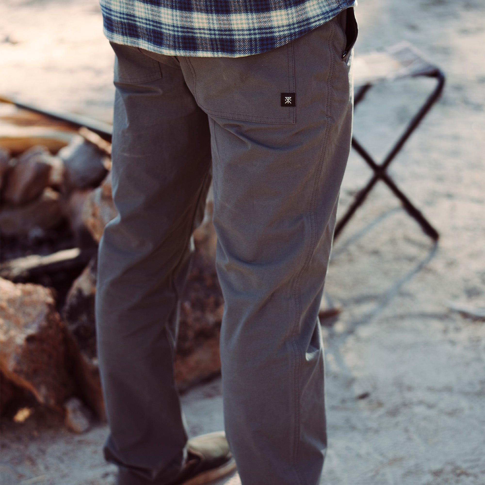 Roark Layover Pro Pants showcased in a dynamic travel setting, featuring a wooden plank and track, emphasizing adventure and mobility.