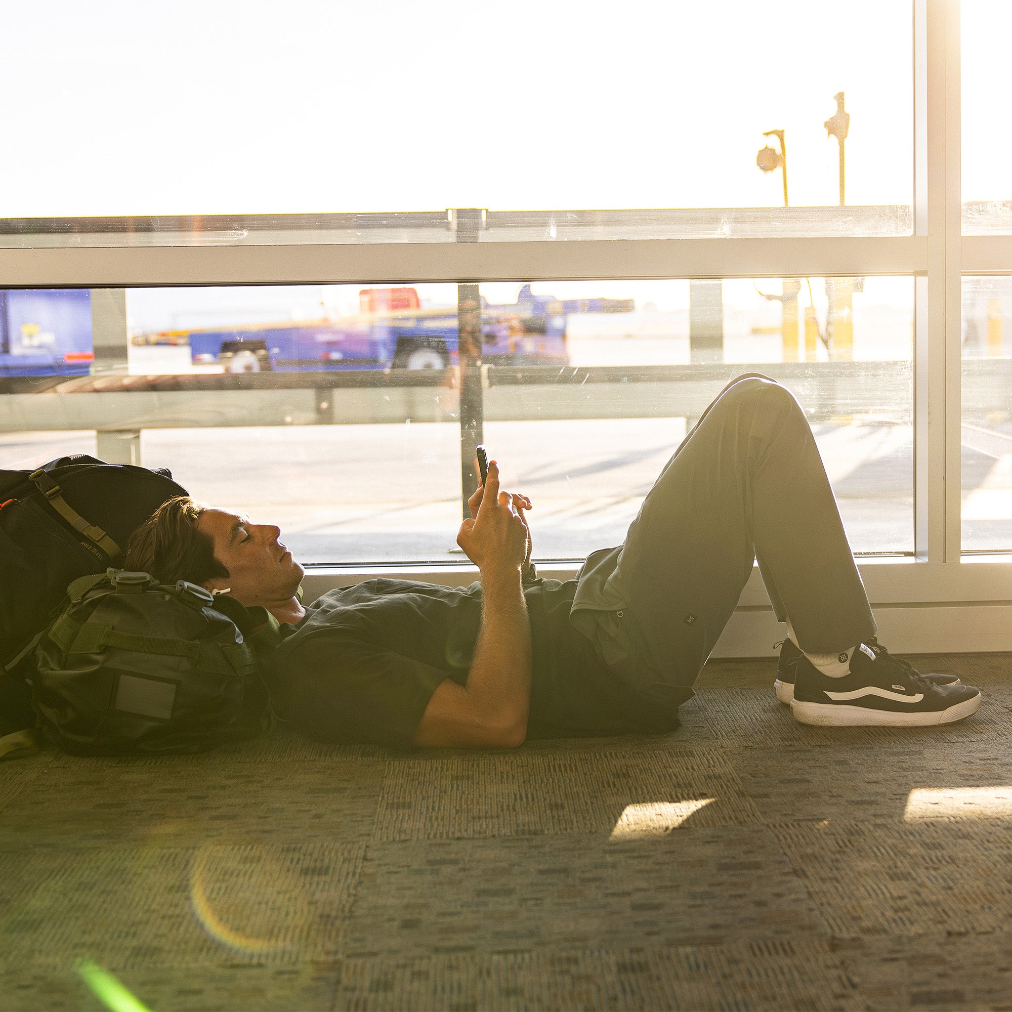 Person sitting casually with stylish sneakers, showcasing the versatility and comfort of Roark Layover Pro Pants, perfect for travel and adventure.