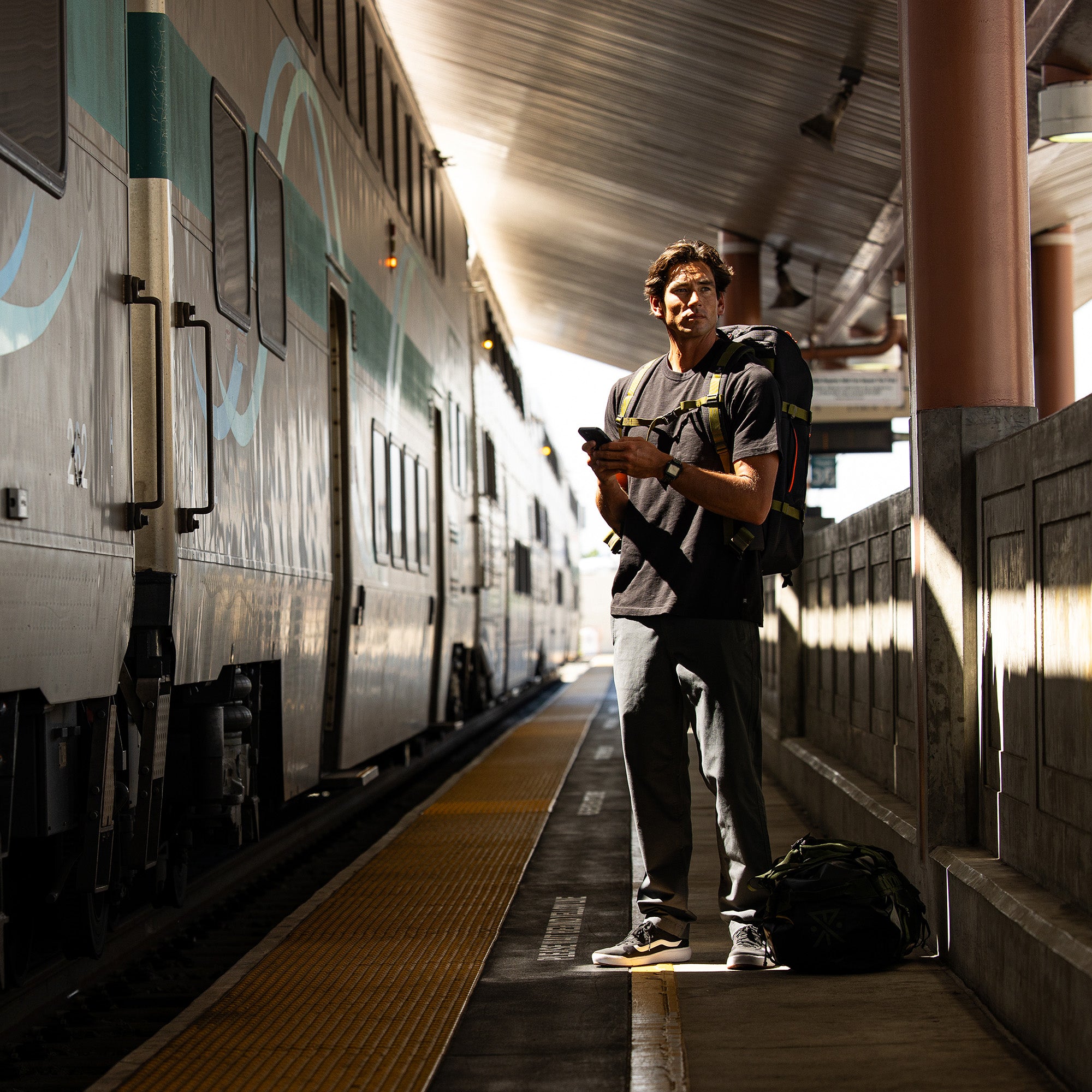 Travel-ready Layover Pro Pants featured in a bustling train station scenario, with a stylish traveler carrying luggage, highlighting their versatility and functionality for adventure and transit.