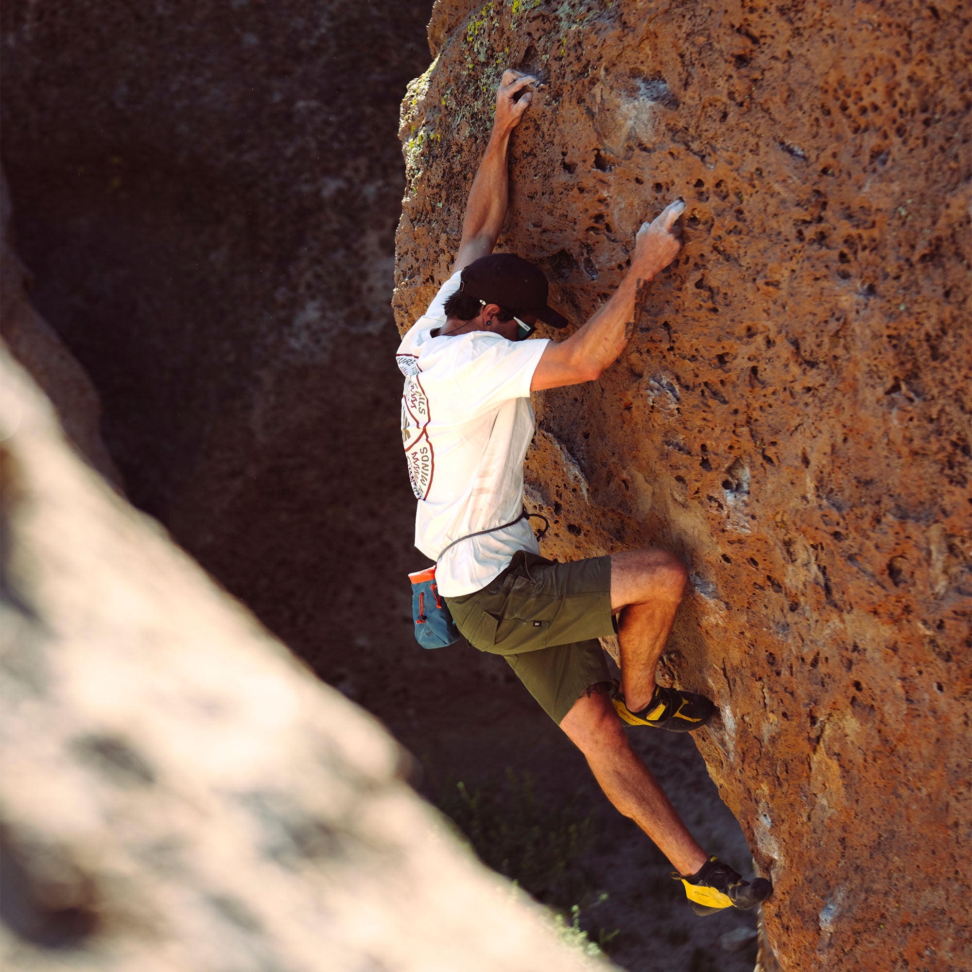 Adventurous rock climber scaling a rugged cliff face, perfectly showcasing the versatility and durability of Roark's Layover Pro Shorts.