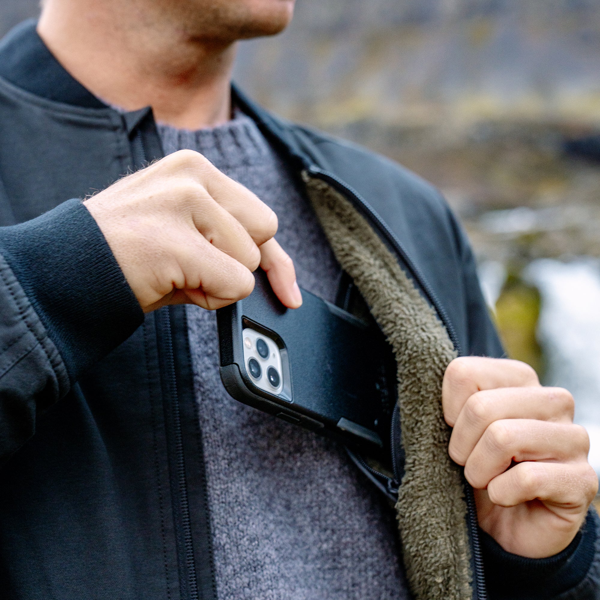 Black layover bomber jacket worn open over gray sweater, showing phone pocket detail on chest