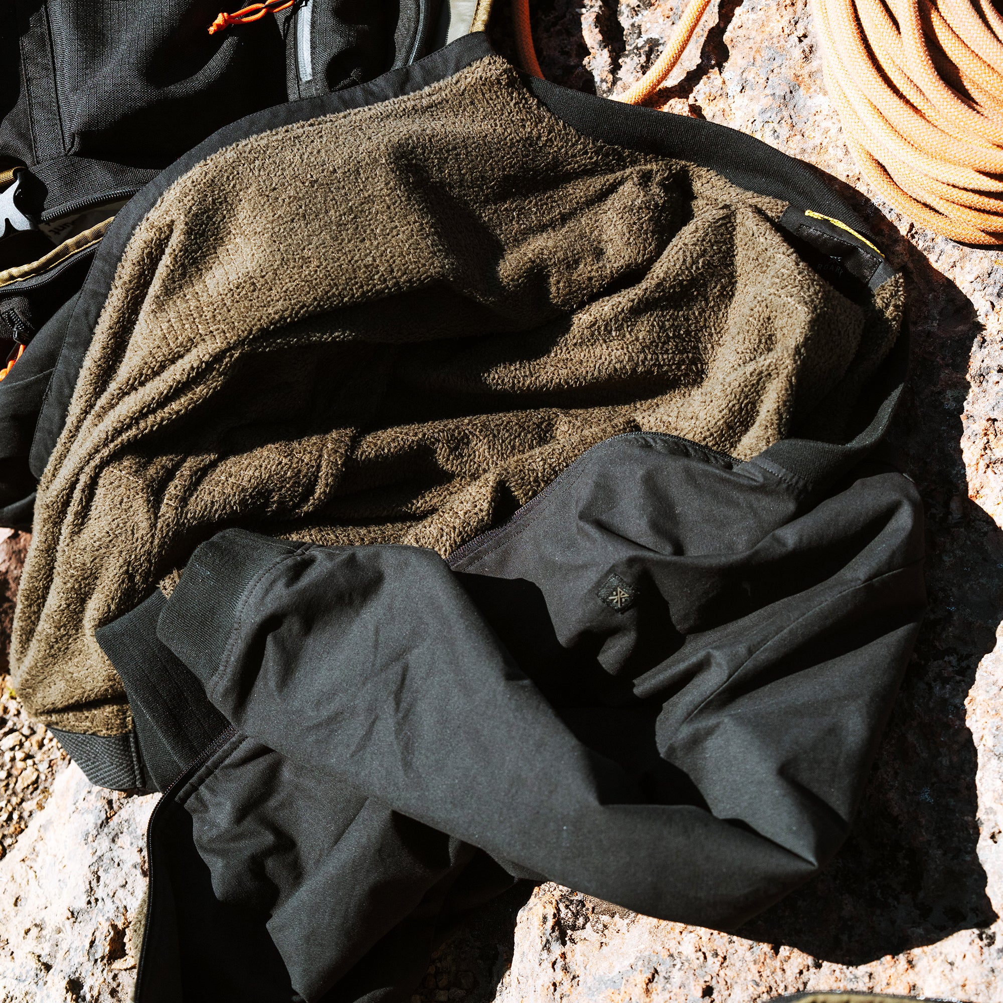 Tan and black textured fabrics folded together outdoors on sandy ground with coiled rope nearby