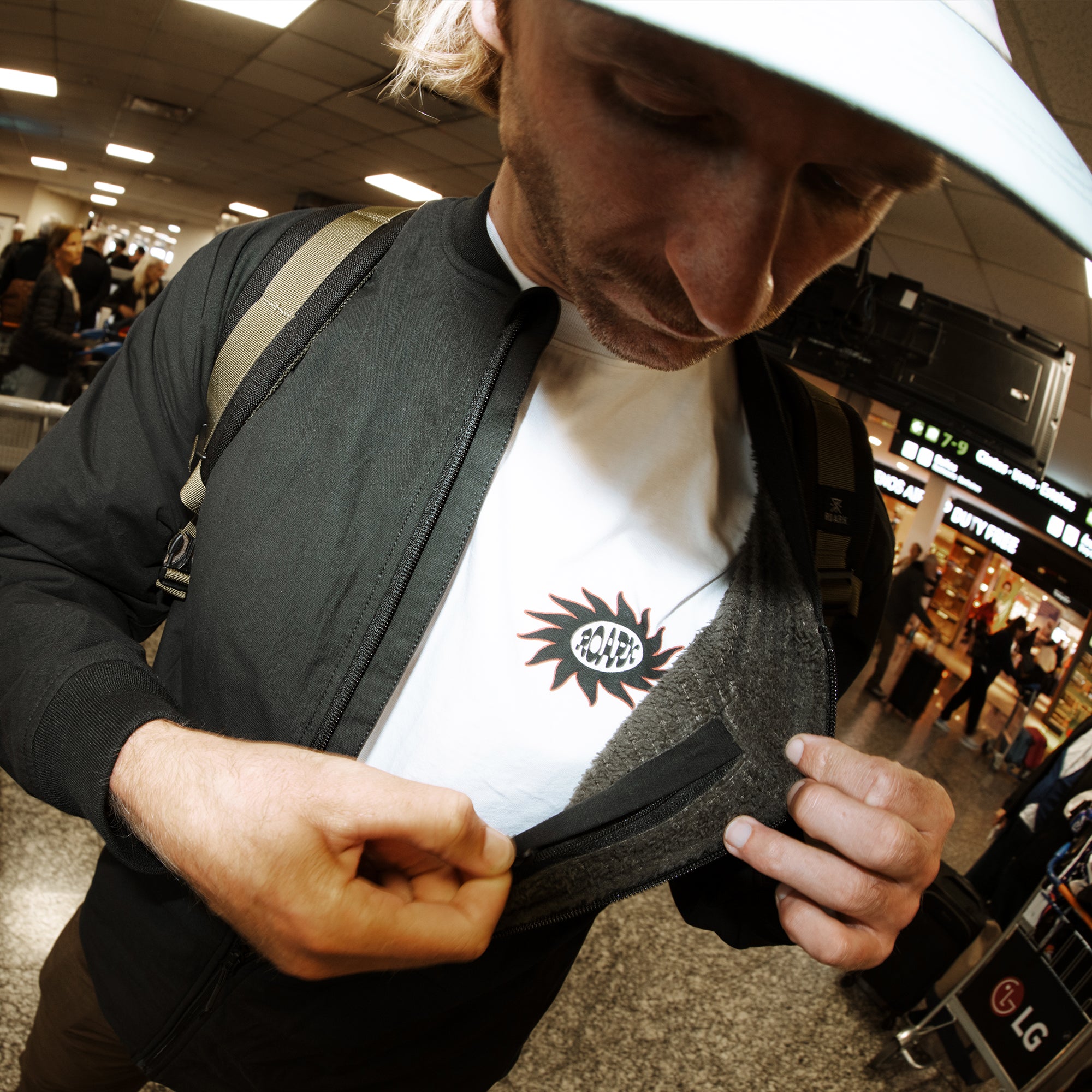 Man wearing black Layover Bomber Jacket with tan stripe and white lining, displaying the sun logo graphic on white shirt underneath