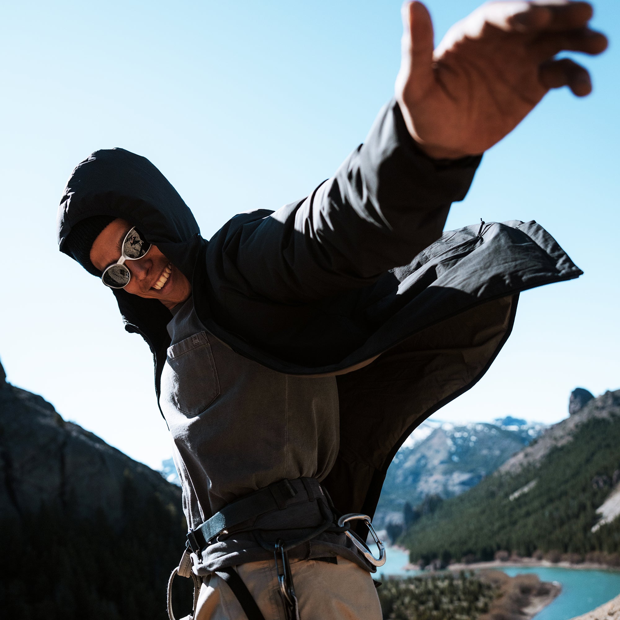 Person wearing black Layover Jacket with white stripe detail over mountains and turquoise lake backdrop