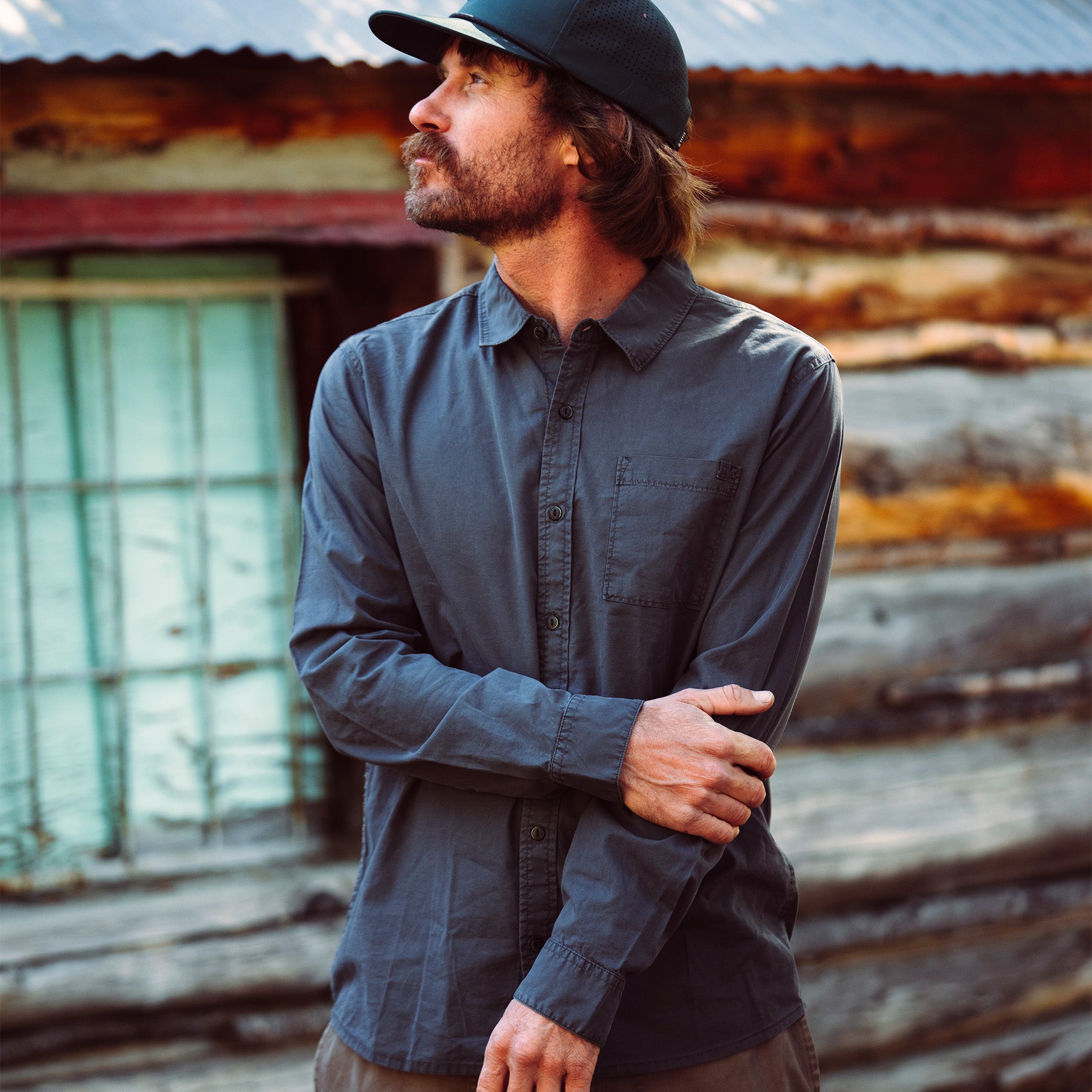 Man in a Made to Fade long sleeve shirt by Roark, styled with a casual hat, emphasizing outdoor adventure and travel style.