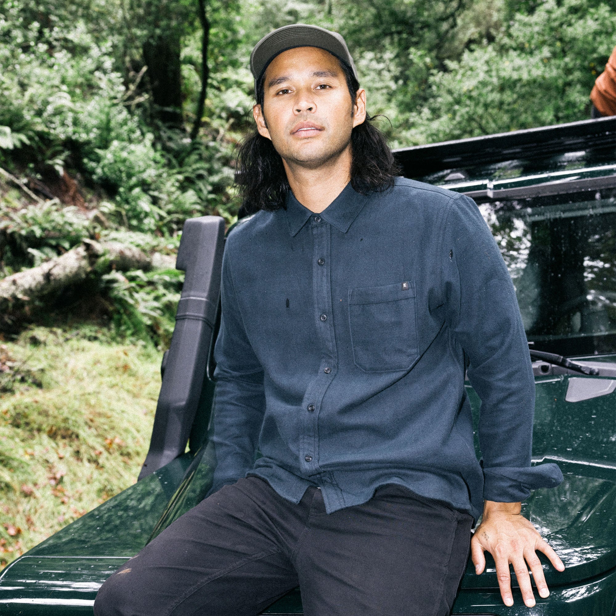 Stylish man wearing a Roark Made To Fade Long Sleeve Button-Up Shirt with collar details, paired with a denim baseball cap, perfect for outdoor adventures and travel.