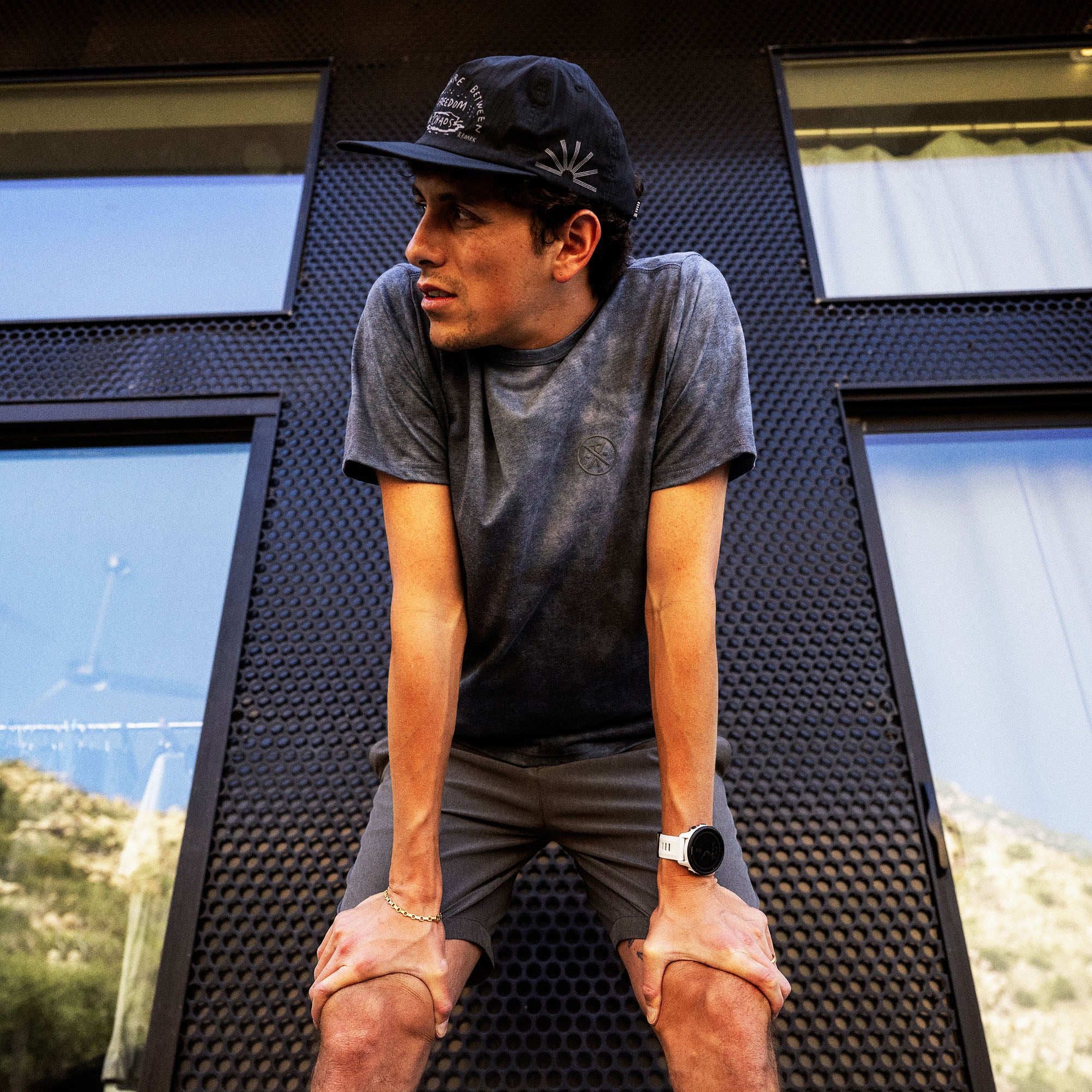 Man wearing charcoal gray short sleeve tee with small chest logo, paired with dark shorts and black cap